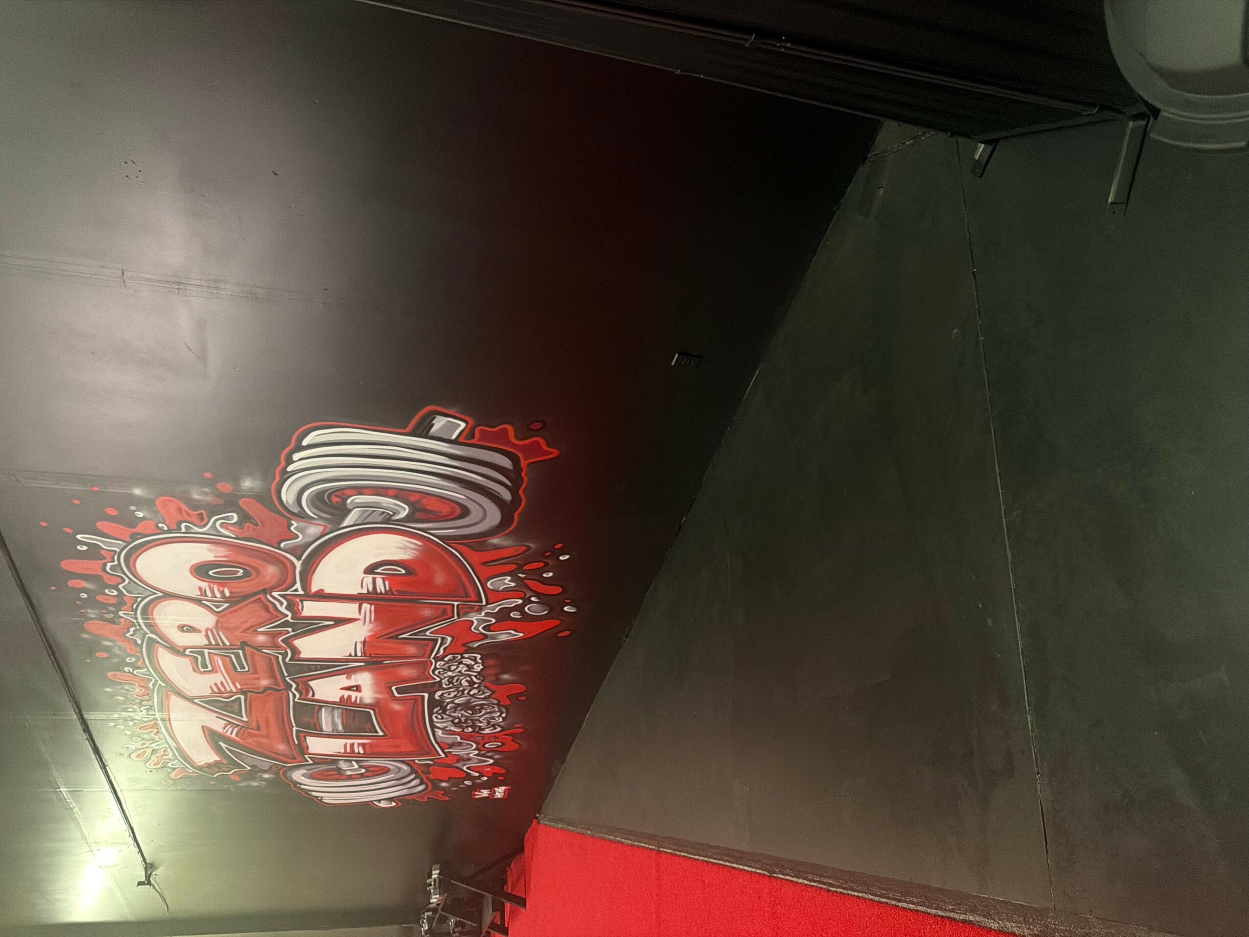 Black wall with red and white graffiti-style text, partially visible, next to a gray floor and a black door frame.