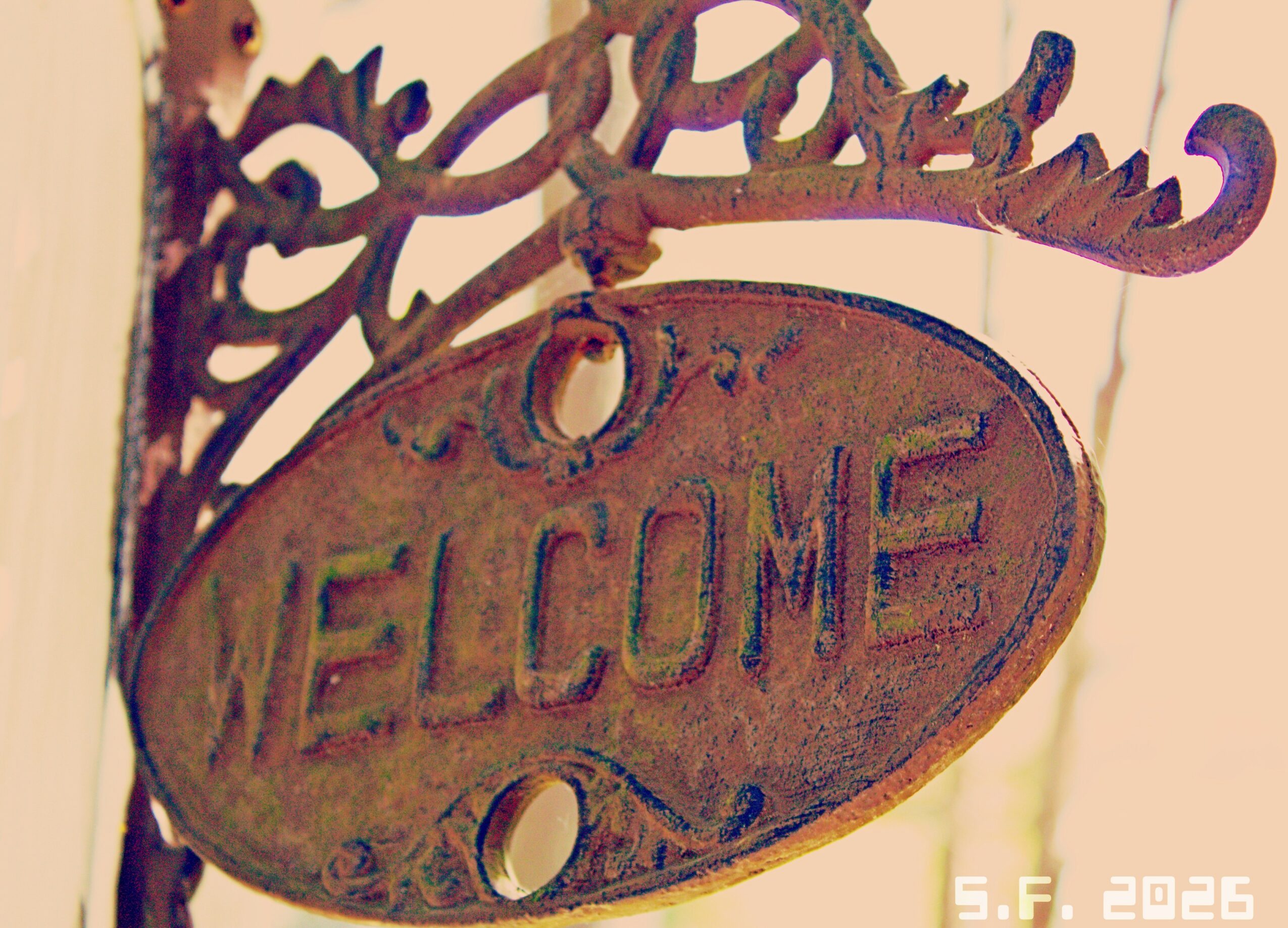 Decorative welcome sign with ornate metalwork, oval shape, and the word 'WELCOME' engraved, hanging on a wall.