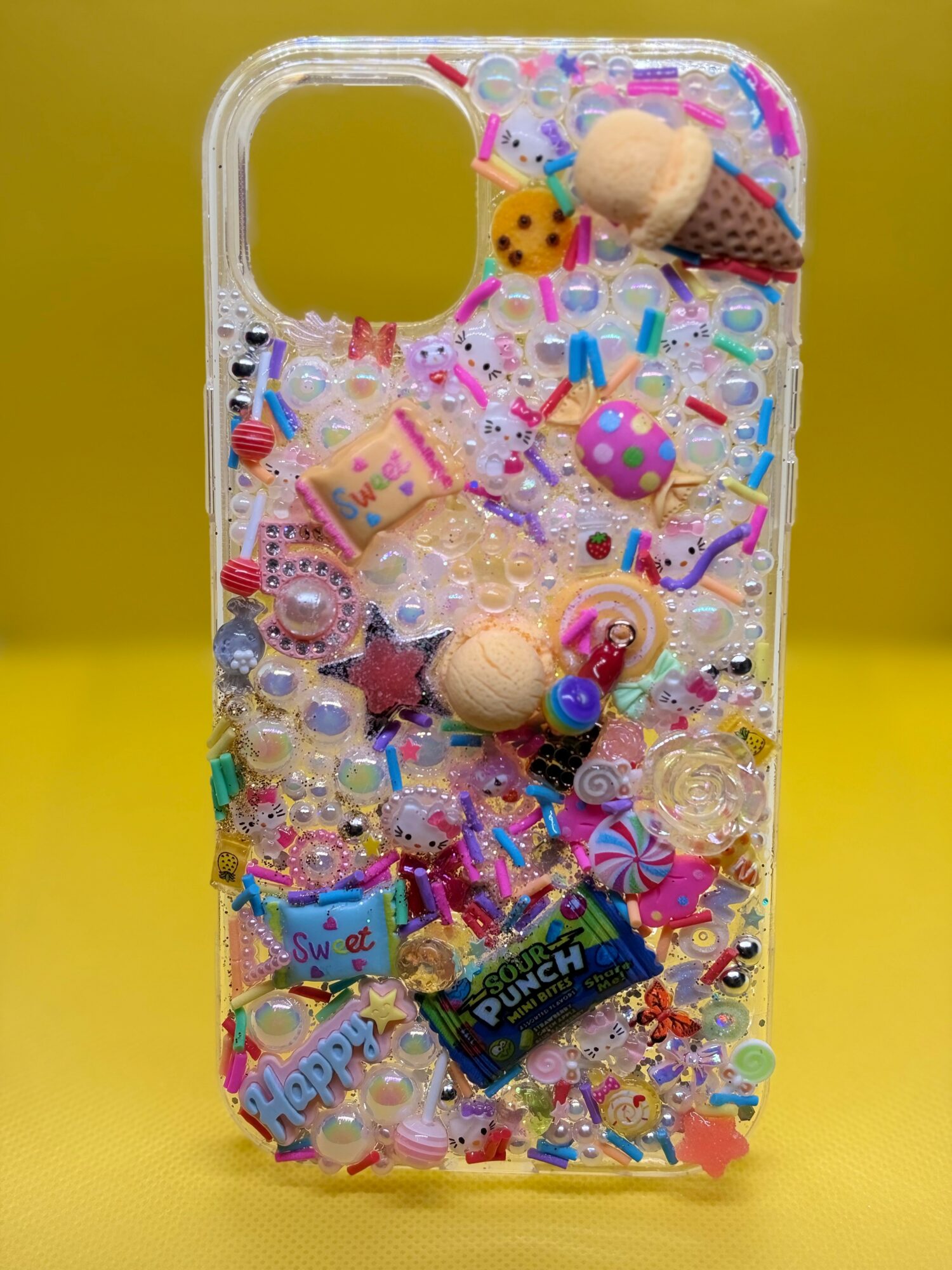 Clear phone case filled with colorful small toys, beads, and candies, against a yellow background.