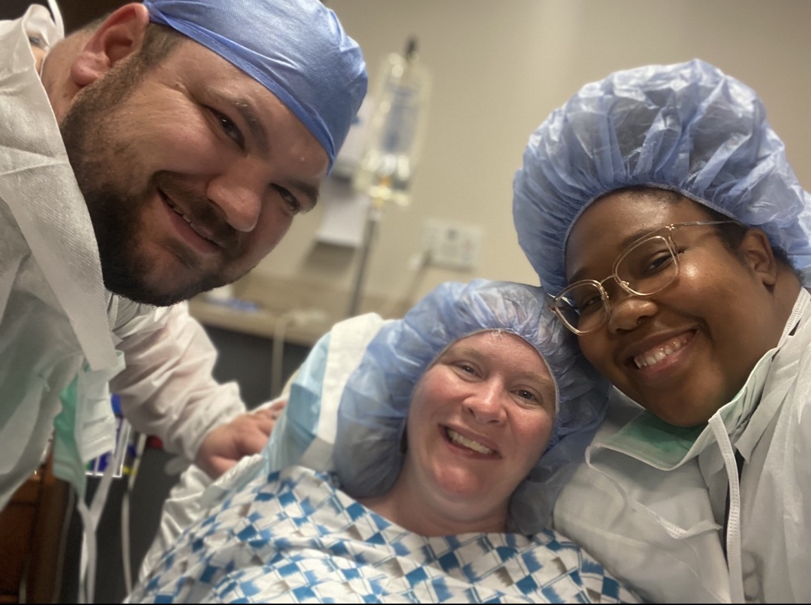 Three healthcare workers in scrubs and caps smiling in a medical setting.