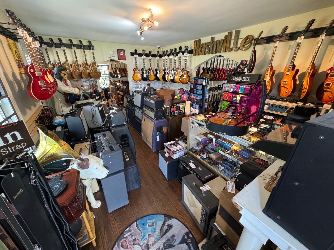 Music store with guitars on walls, shelves, and counters, and various electronic equipment inside.