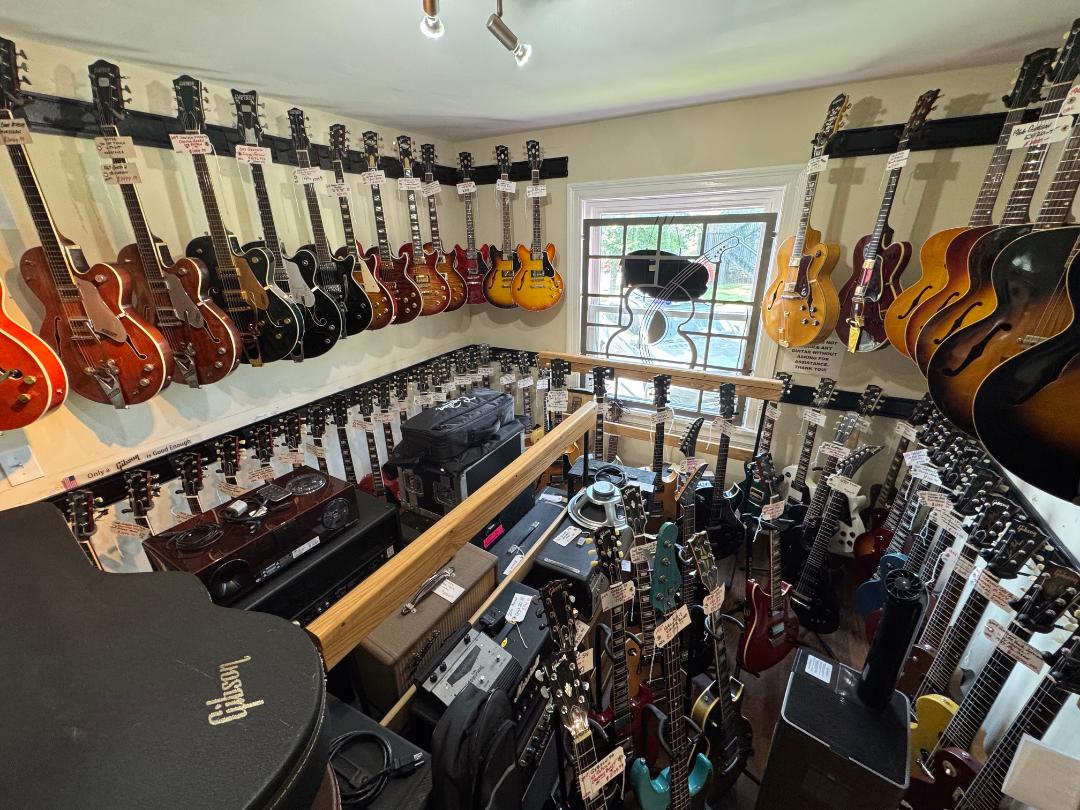 Room filled with guitars hanging on walls, with a window and musical equipment below, viewed from above.