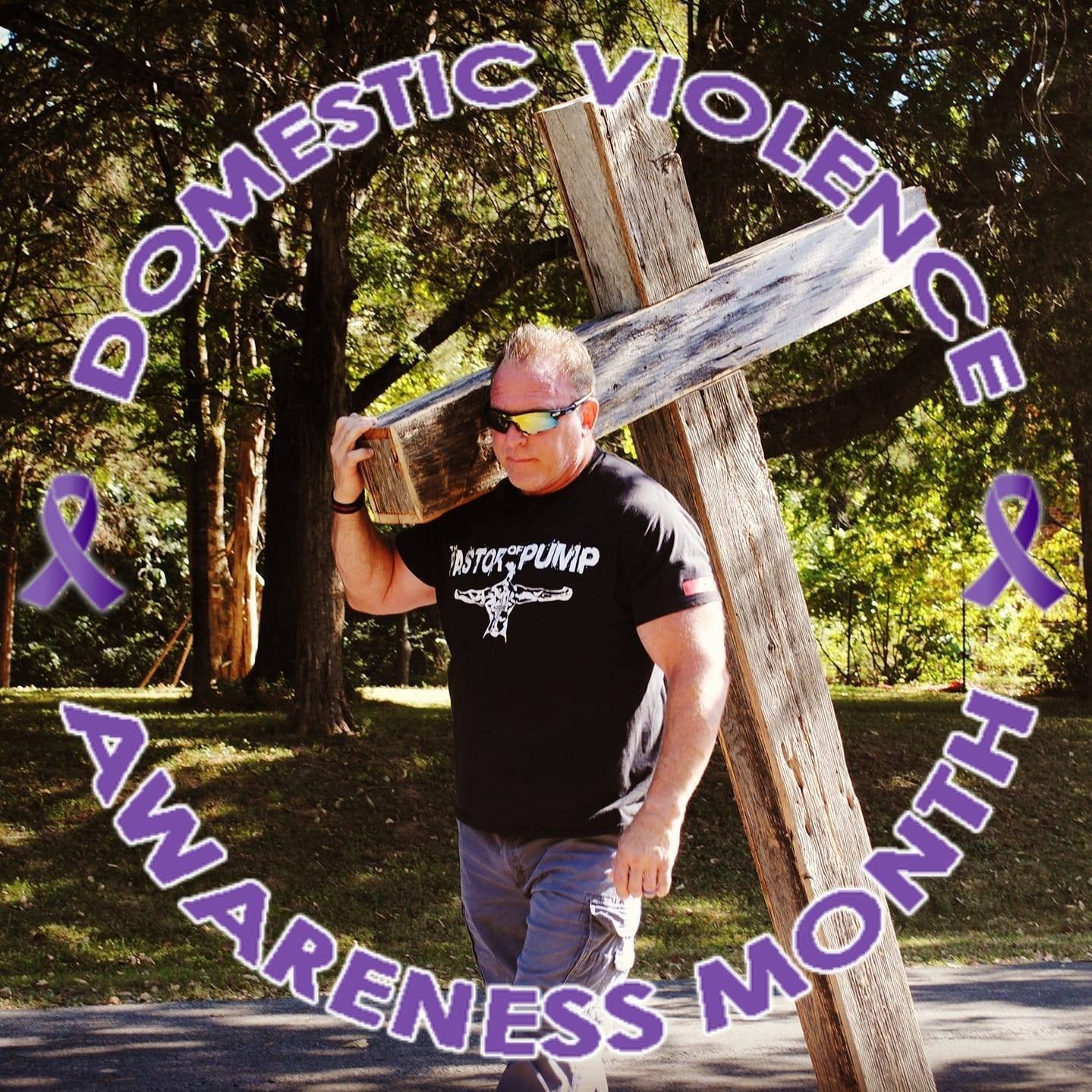 Person carrying a wooden cross outdoors with trees in the background, surrounded by purple awareness ribbons and text about domestic violence awareness month.