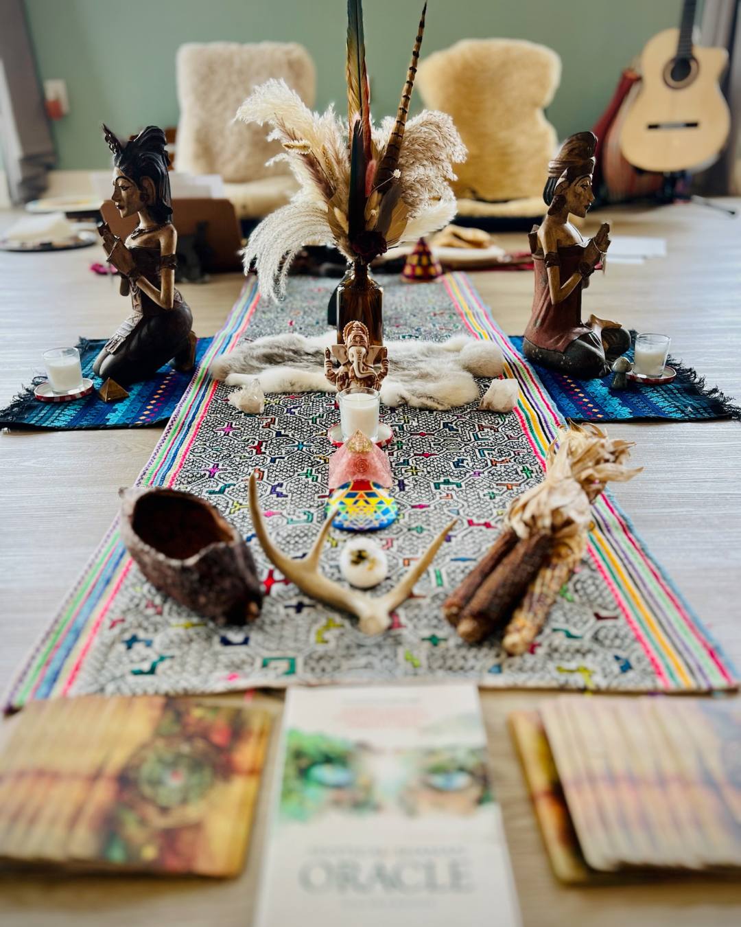 Decorative arrangement with figurines, a mouse, and books on a colorful rug in a room with a guitar and chairs in the background.