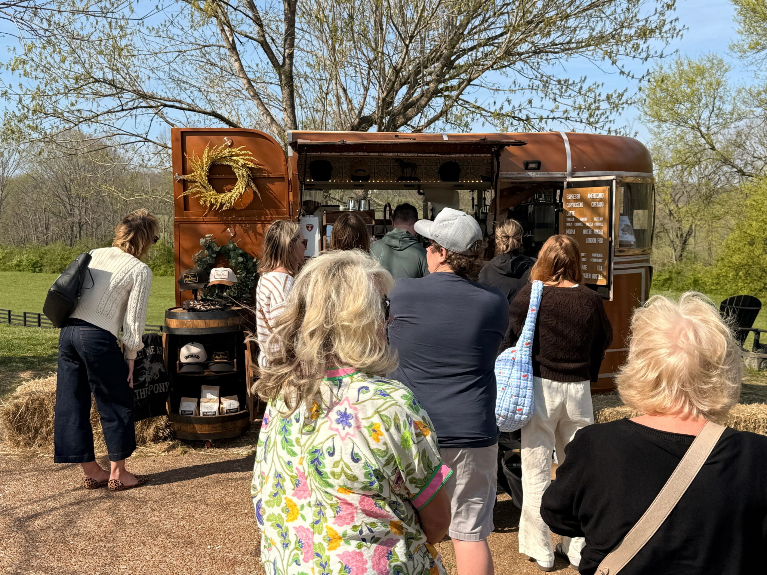 People gather around a food truck outdoors with trees and grass in the background.