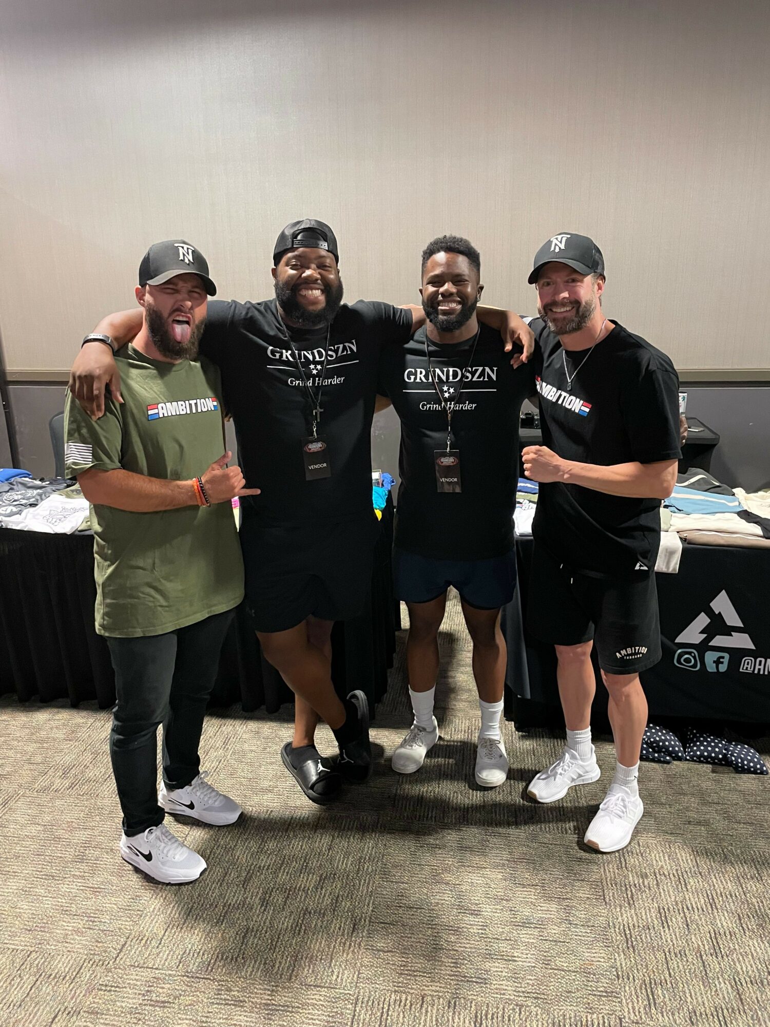 Four people standing together indoors, three wearing black sportswear and one in a green shirt, smiling and posing for a photo.