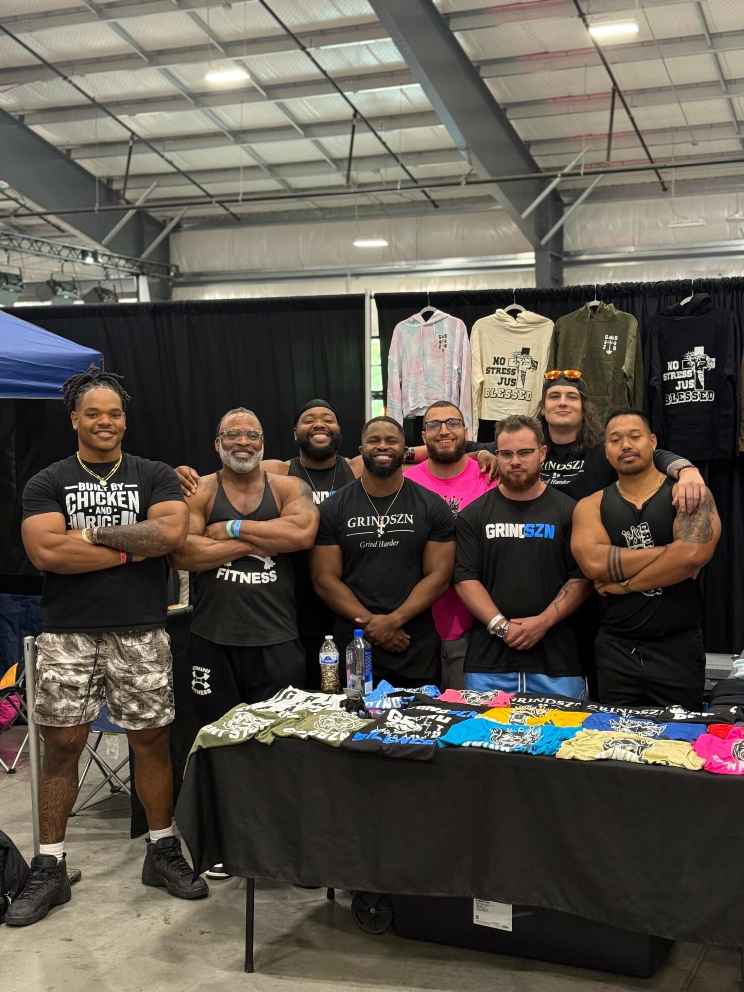 Group of nine people standing behind a table with clothing items in an indoor venue.