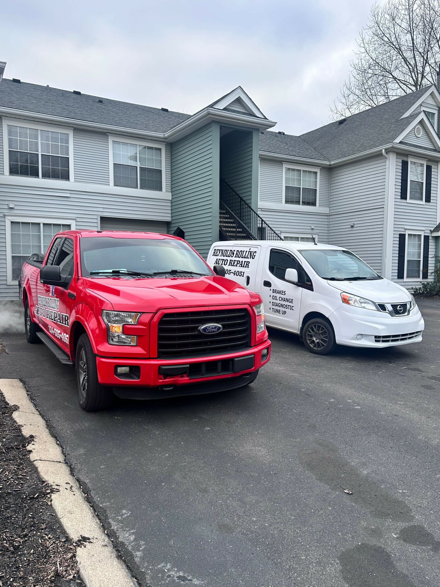 Three parked cars in front of a residential building, one red and two white, on a paved driveway.