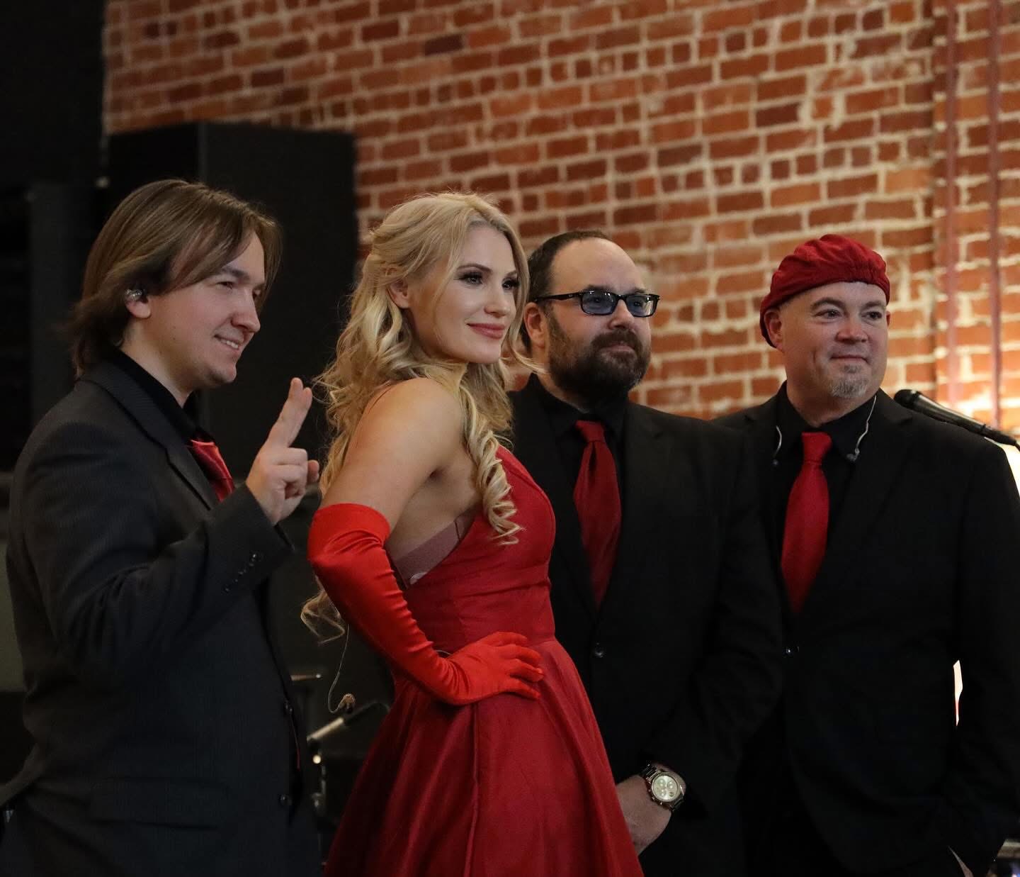 Four people dressed in formal attire, standing against a brick wall, smiling and posing for a photo.