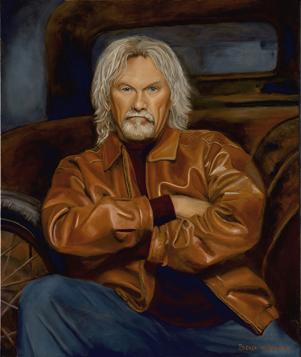 Portrait of an older man with long gray hair and beard, wearing a brown leather jacket, sitting with arms crossed.