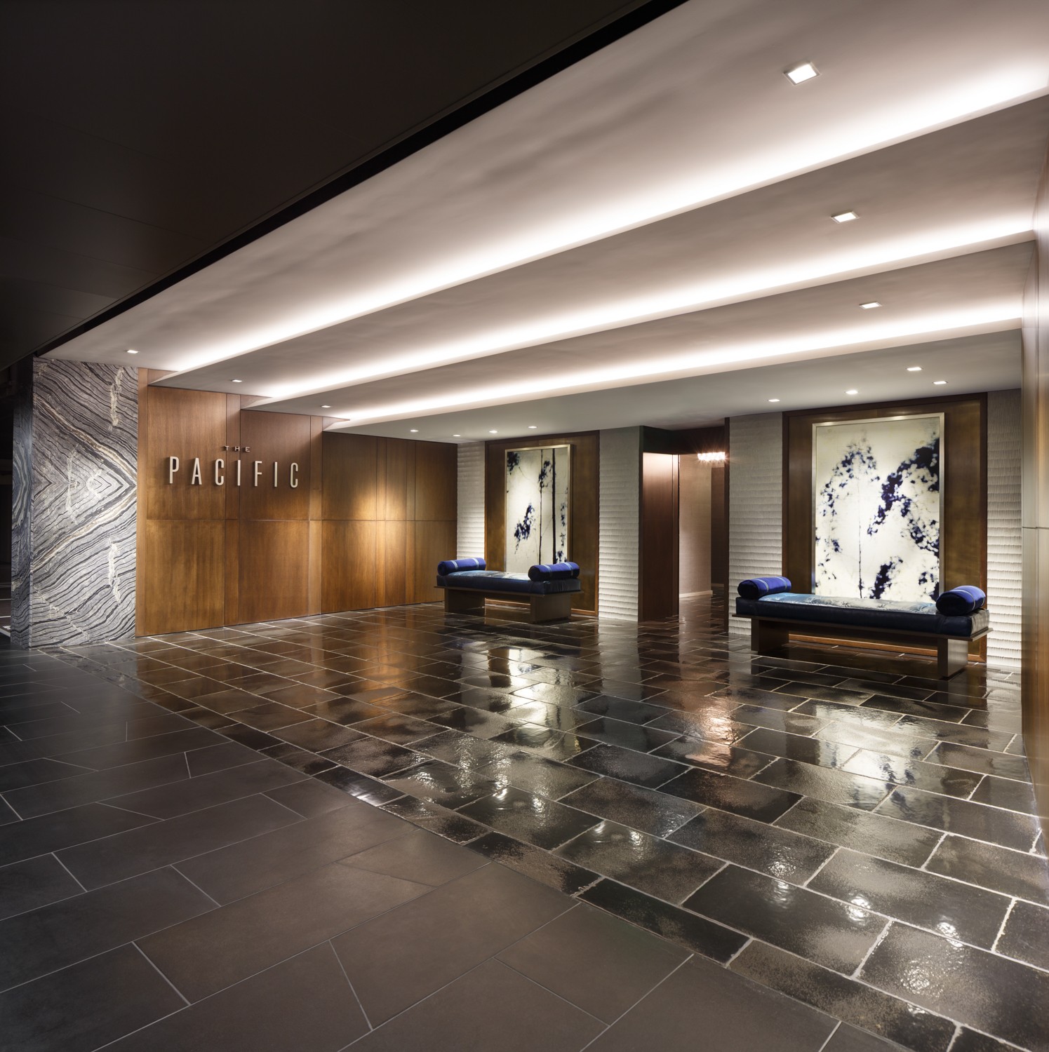 Lobby with wooden wall, illuminated ceiling, two art displays, and benches, reflecting a modern interior design.