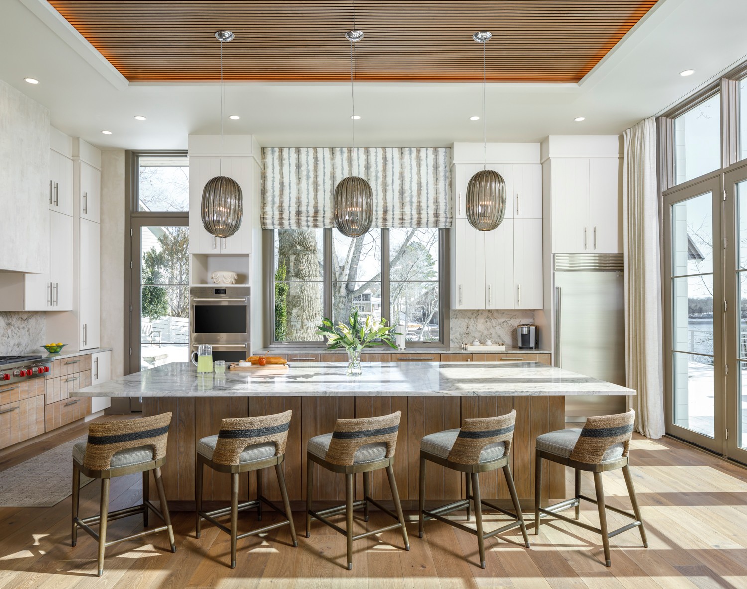 Modern kitchen with white cabinets, a large island, bar stools, and large windows with a view outside.