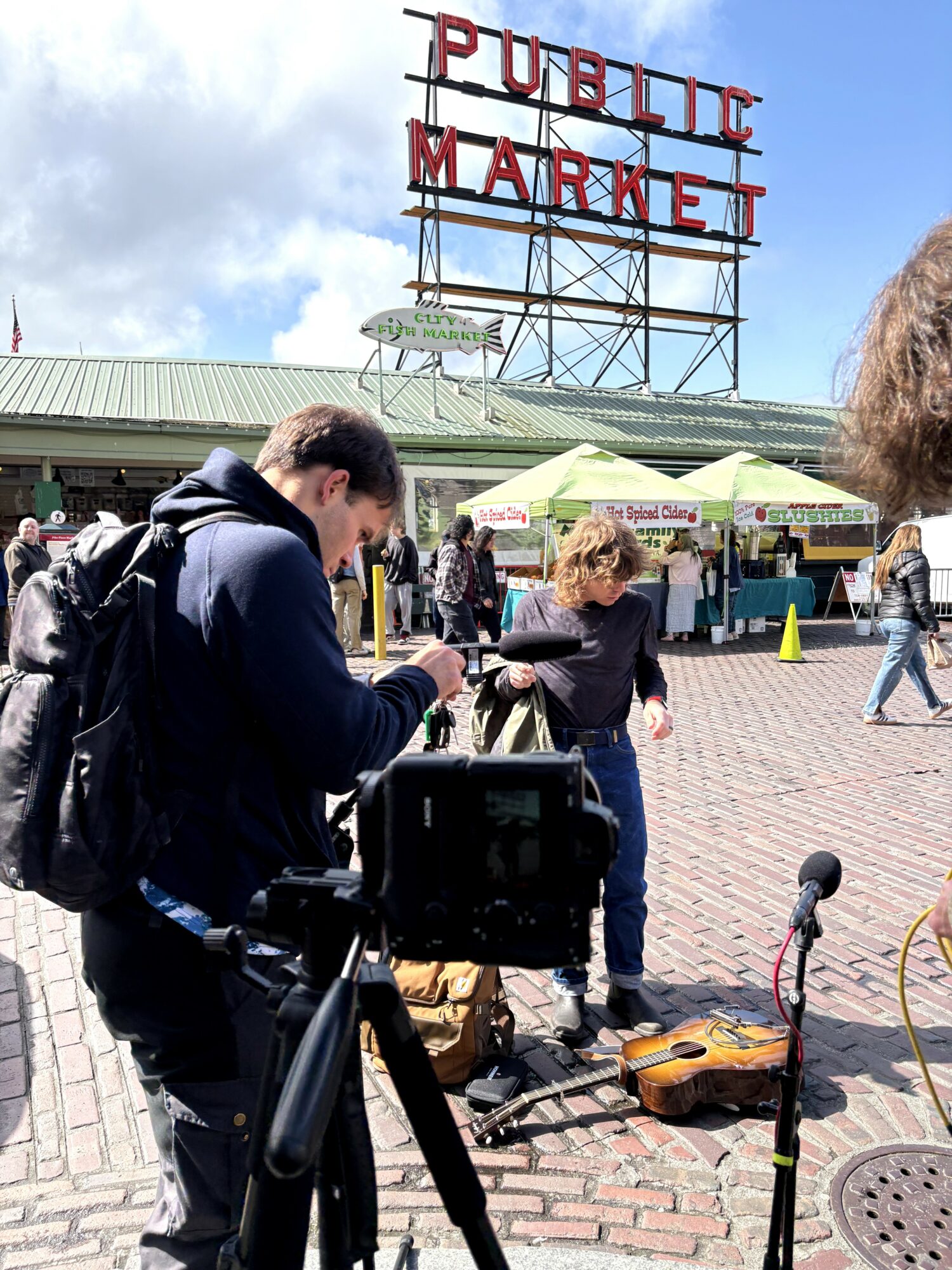 People gather outside a public market with a large sign reading 'PUBLIC MARKET' on a cloudy day.