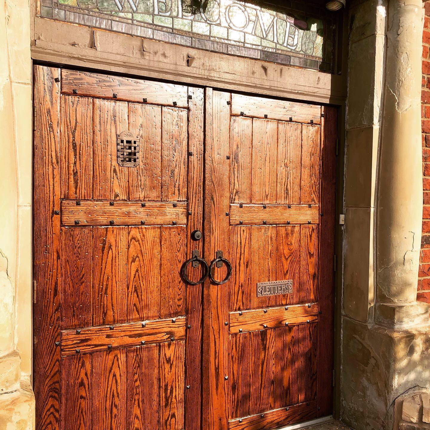 Wooden double door with metal rings as handles, set in stone frame, with a small metal sign on the right door.