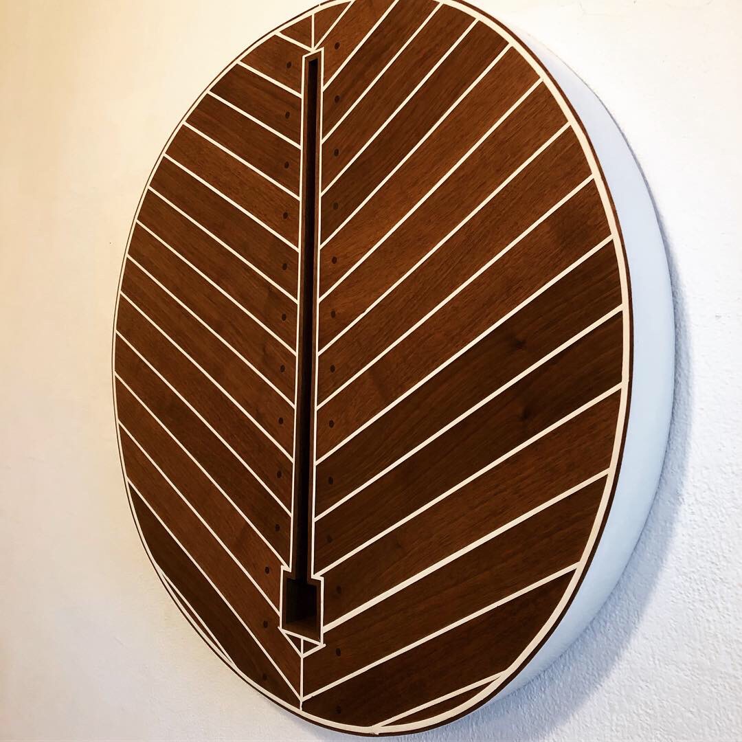 Round wooden clock with a vertical black line and diagonal lines, mounted on a white wall.