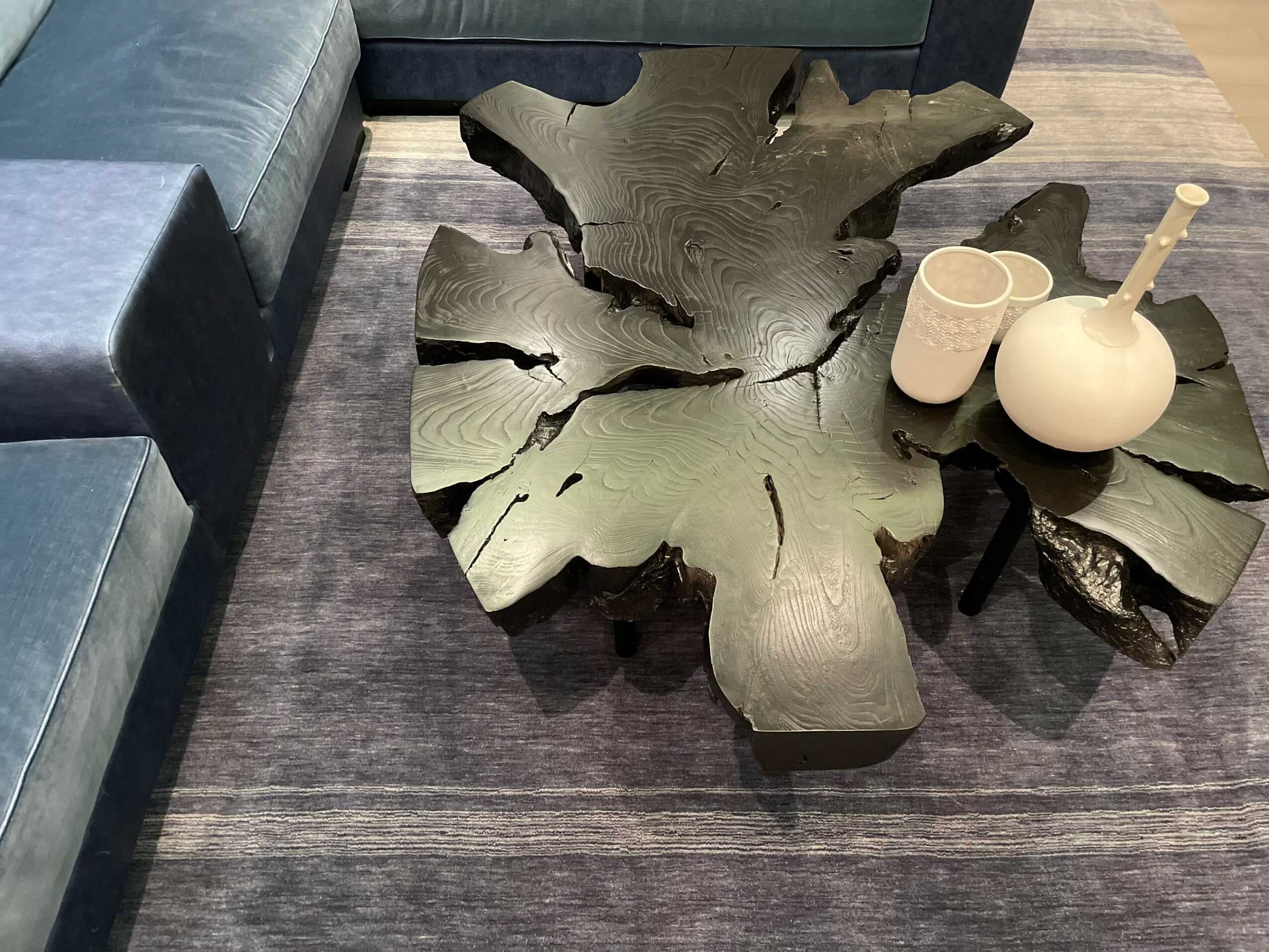 Two wooden tables with natural, irregular shapes and cracks, placed on a gray rug, with vases on one table.