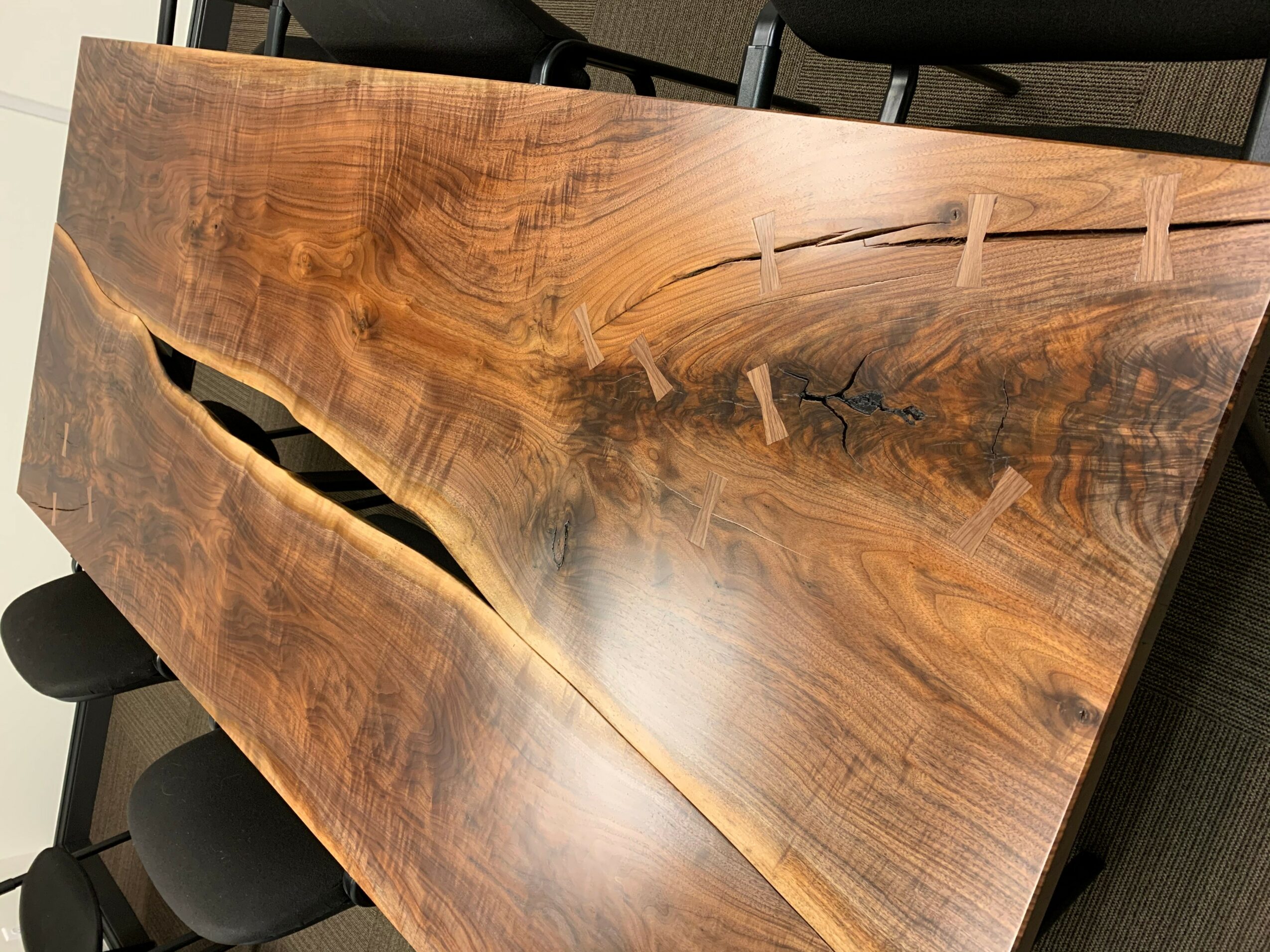 Wooden table with a natural crack and a glossy finish, surrounded by chairs, viewed from an angle.