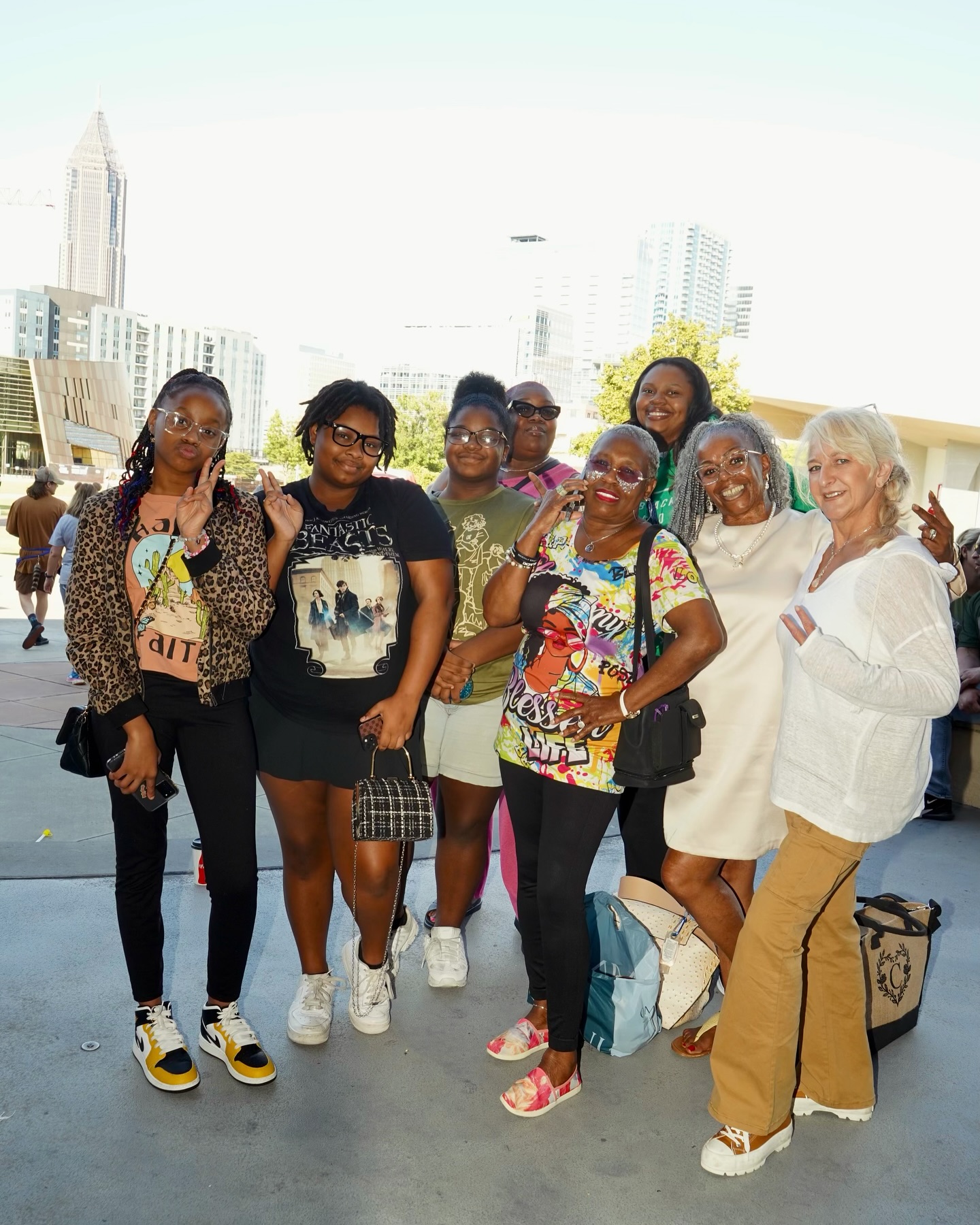 Group of seven women standing outdoors in a cityscape, smiling, with tall buildings in the background.