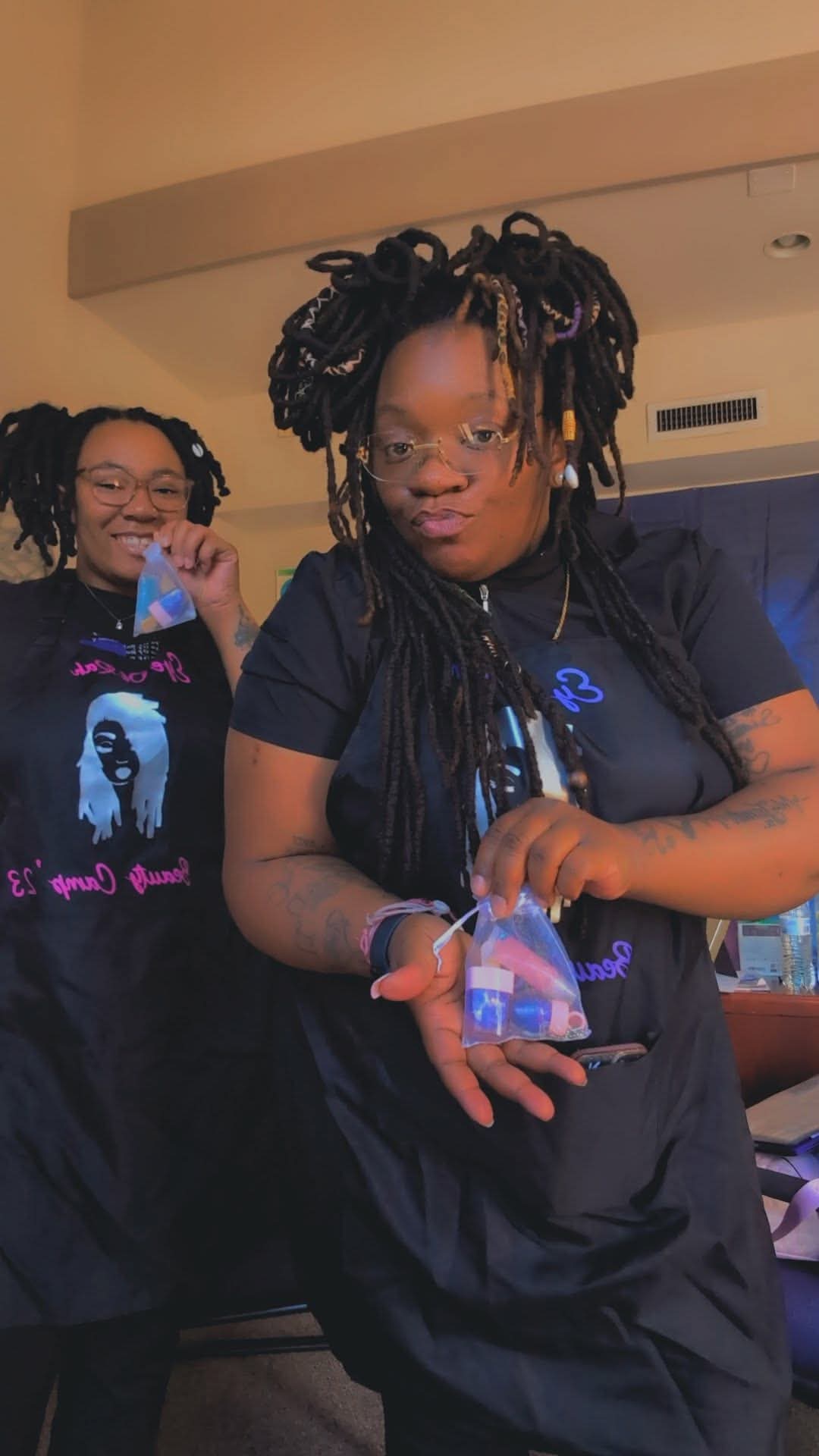 Two women with styled hair, one holding a small object, in an indoor setting, smiling and looking at the camera.