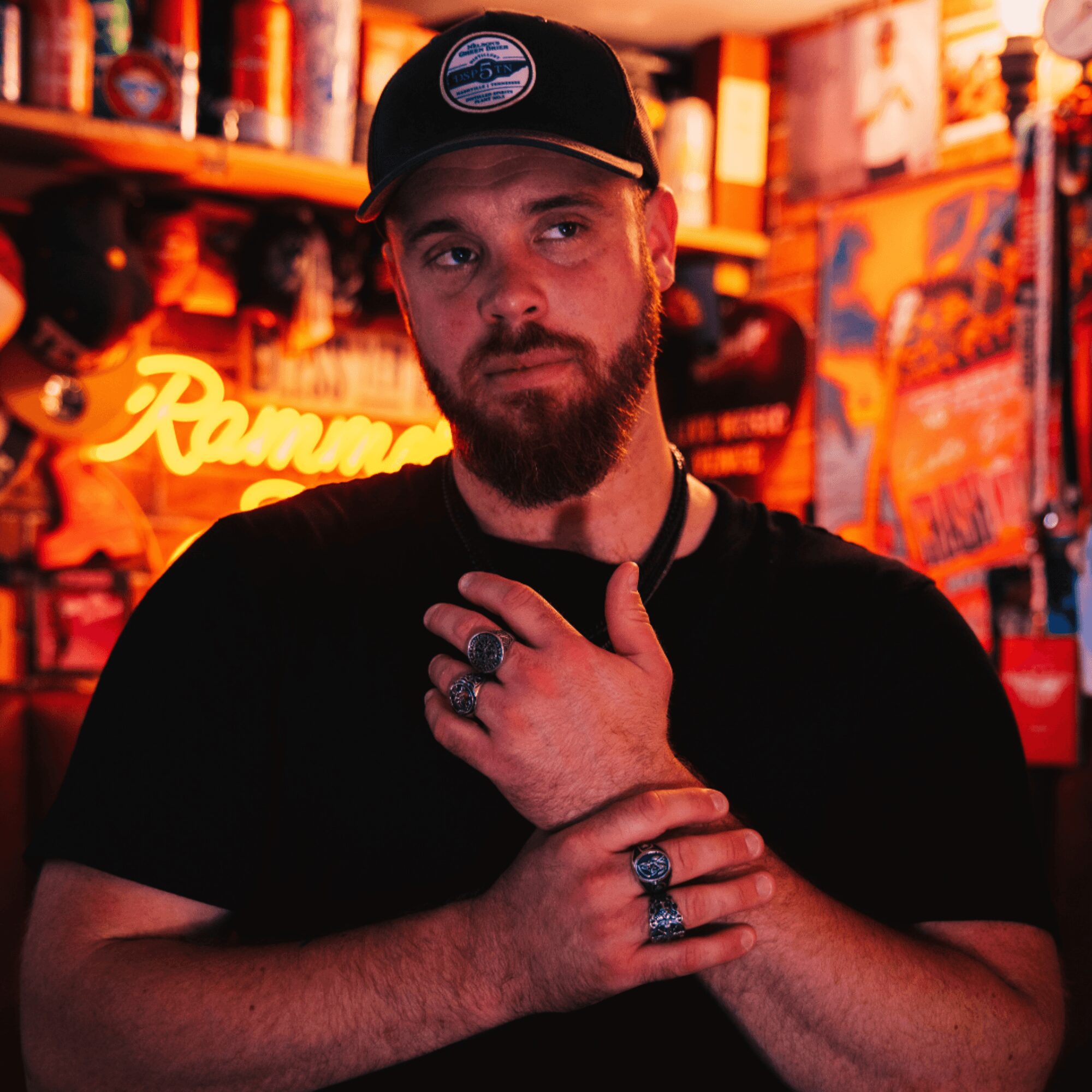 Man with beard and rings, wearing a black cap and shirt, in a colorful bar or restaurant setting.