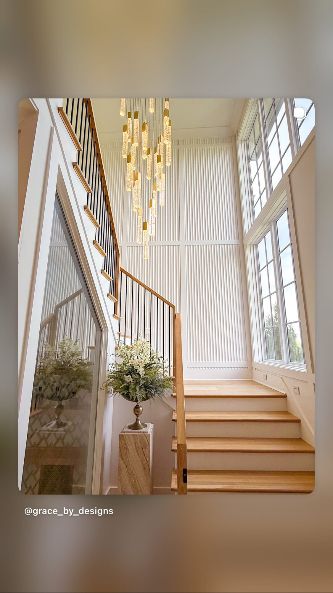 Interior view of a staircase with wooden steps, large windows, and a modern chandelier, bright and airy space.
