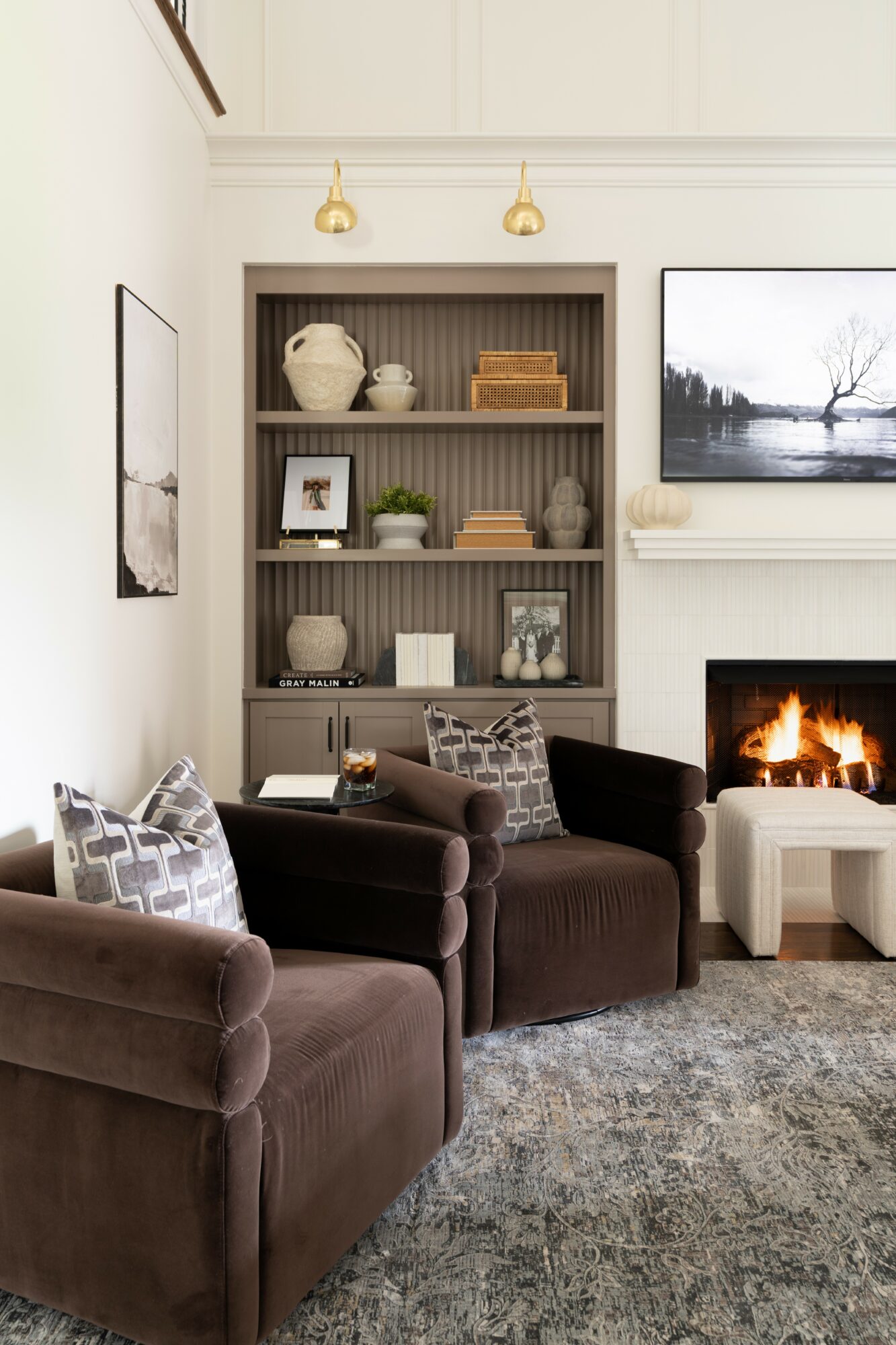 Living room with dark brown sofas, a fireplace, a tall bookshelf, and wall art, with a rug on the floor.