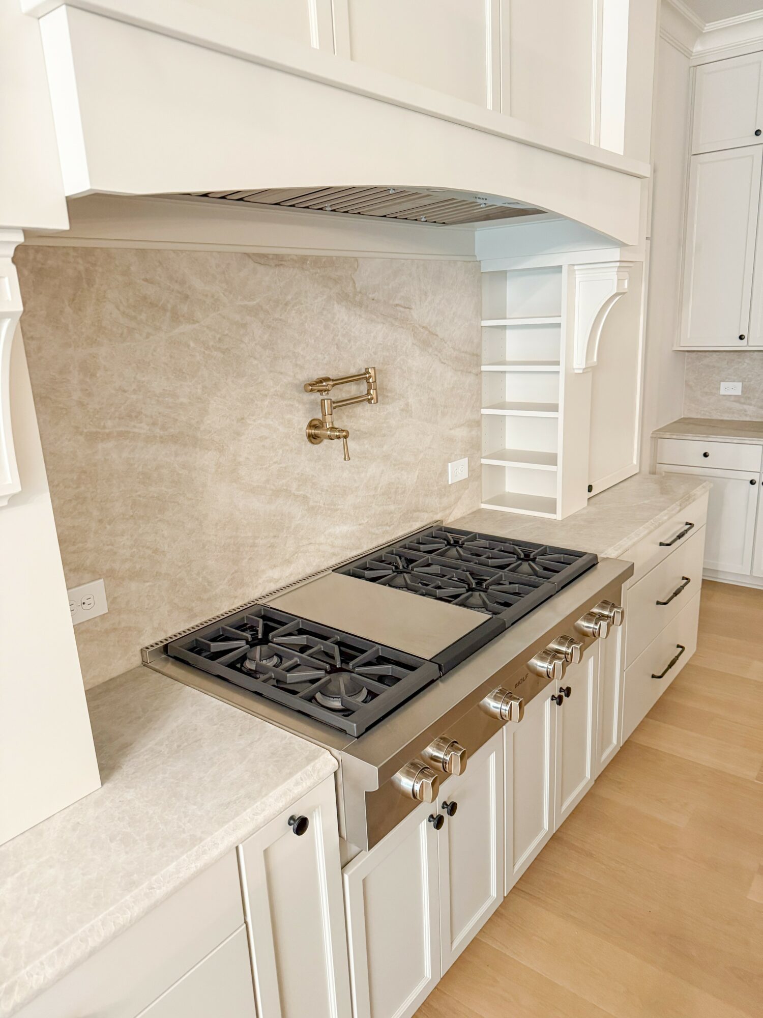 Kitchen with a stove, beige backsplash, white cabinets, and a light-colored countertop, viewed from the side.