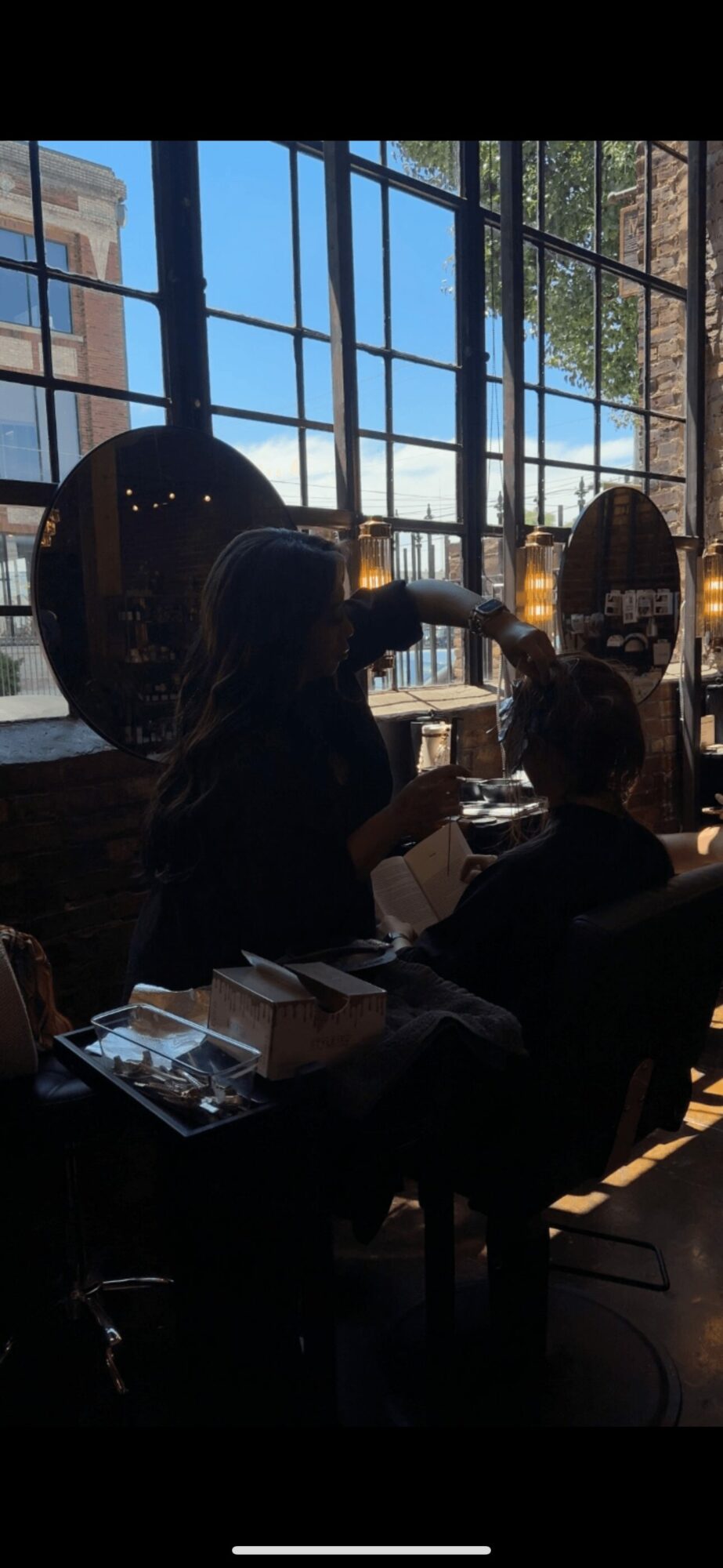 People sitting at a table near large window with a view of buildings outside, sunlight streaming in.