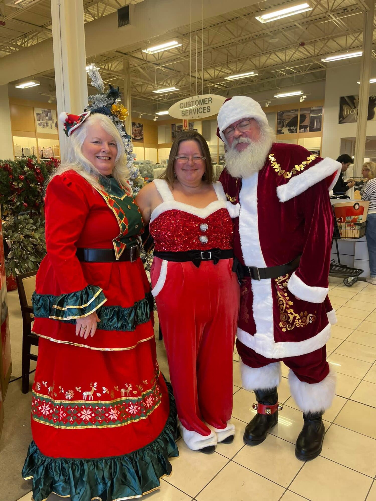 Three people dressed in festive costumes standing inside a store, smiling, with Christmas decorations in the background.
