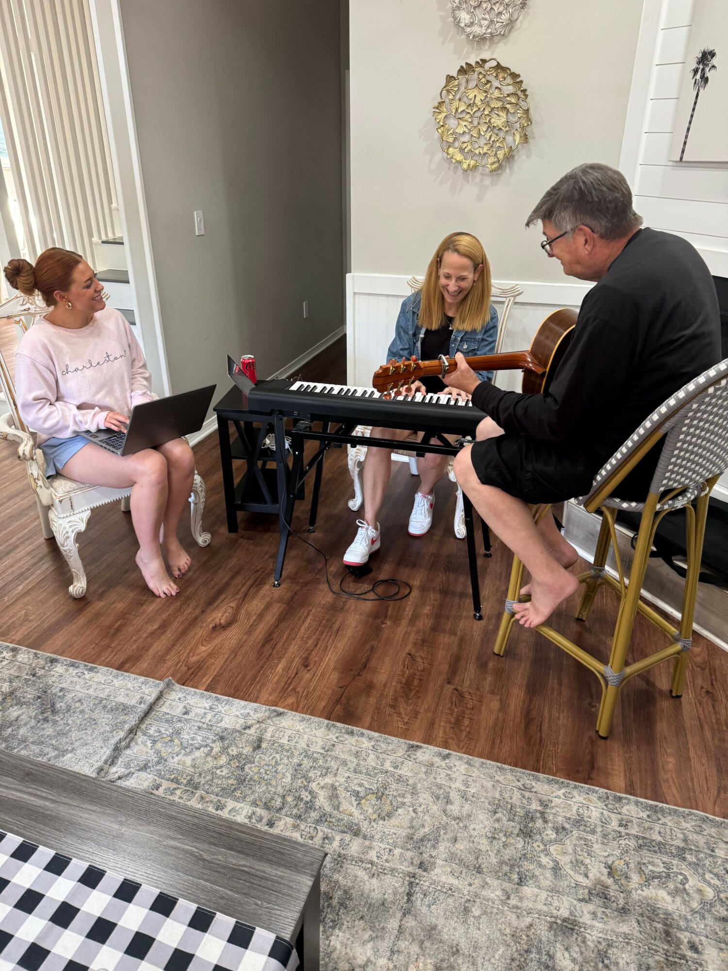 People gathered around a keyboard and a laptop in a room with wooden flooring and decorative wall art.