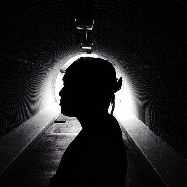 Silhouette of a person with pointed ears in a tunnel with bright light behind, side profile, dark surroundings.