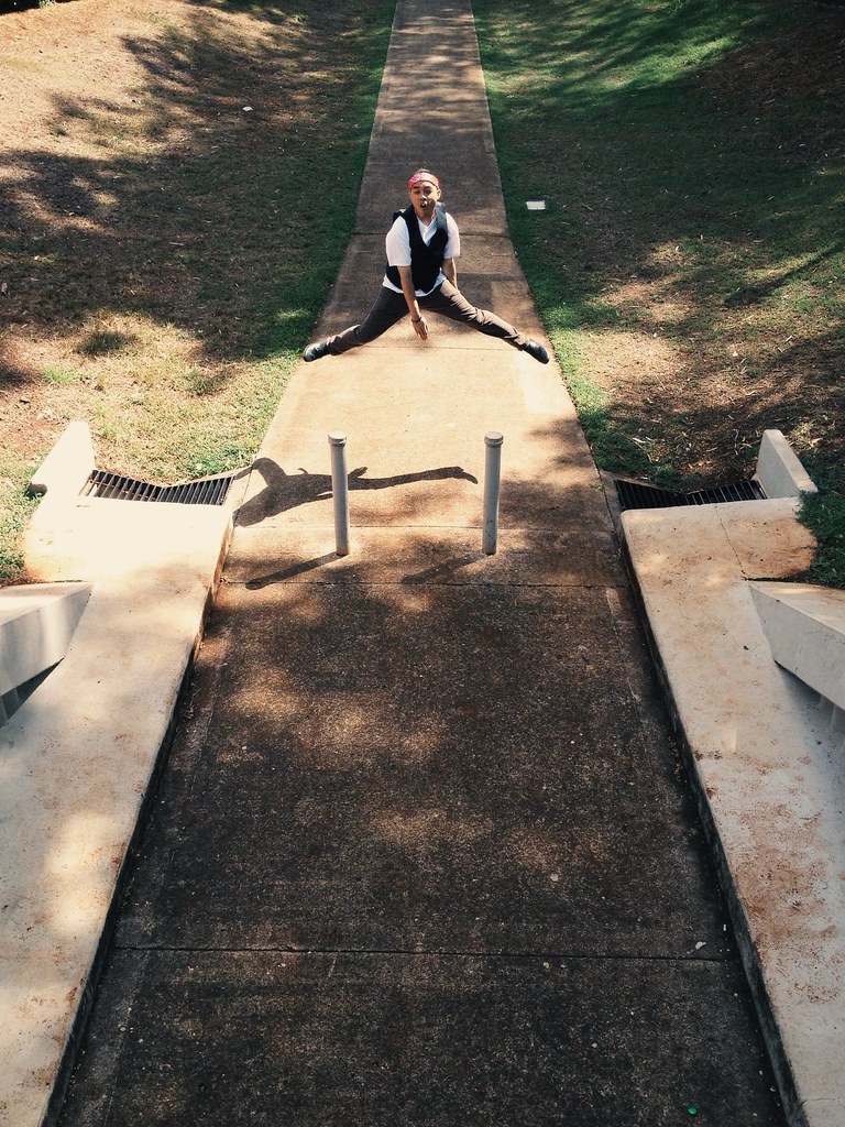 Person sitting on a concrete ledge at the end of a pathway in a park, with grass and trees around.