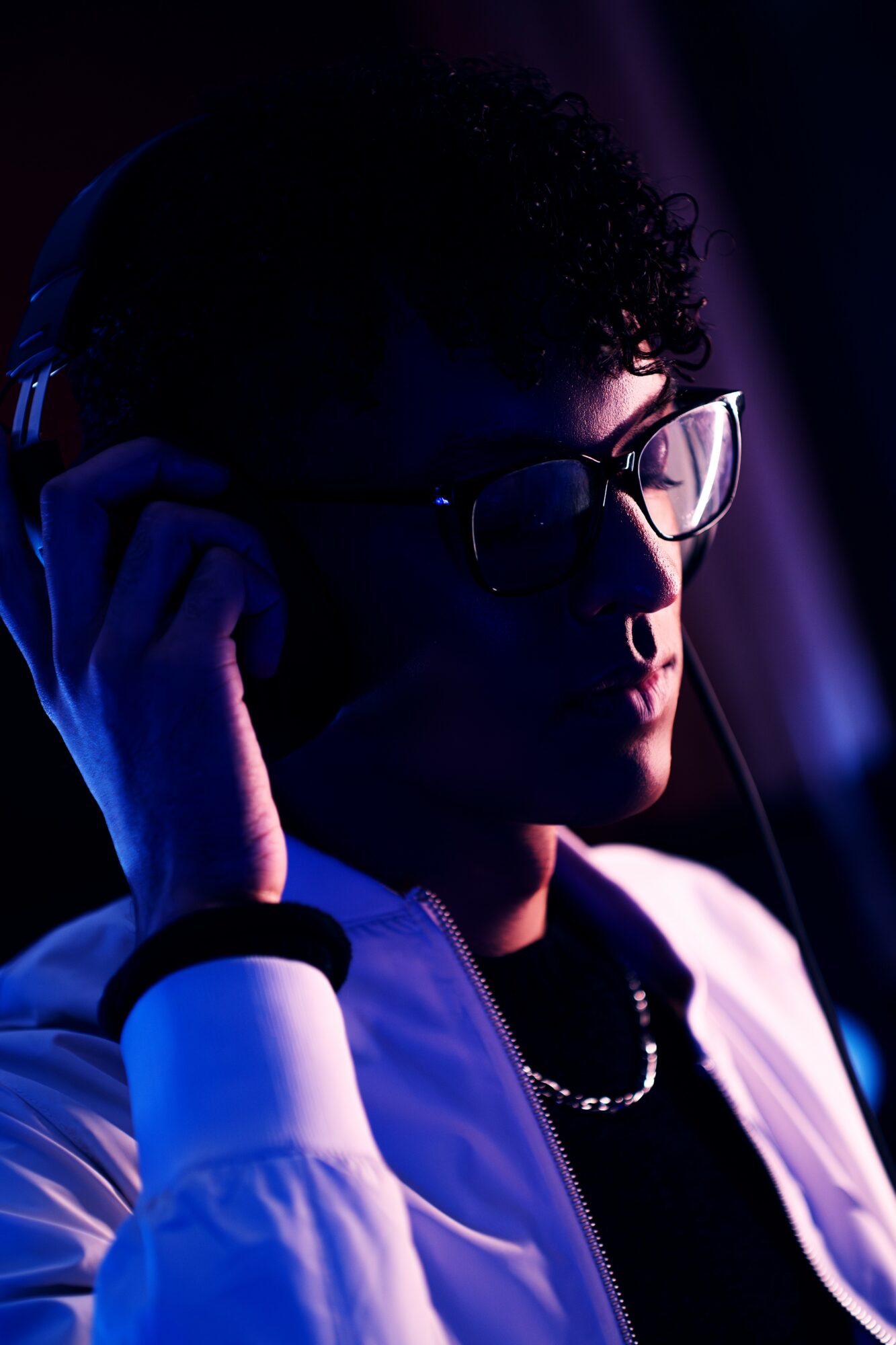Person wearing glasses and headphones, in a dark setting with purple lighting, adjusting headphones, face partially visible.