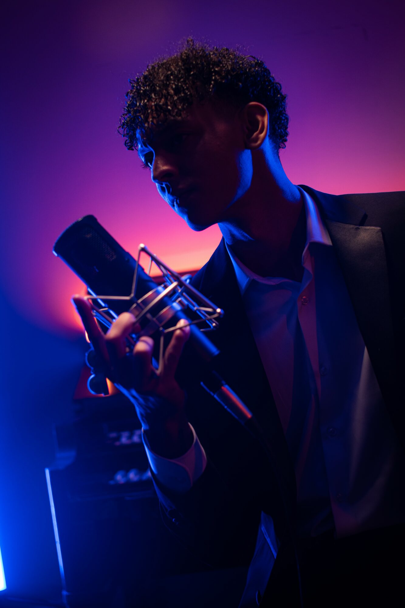 Person with curly hair in a suit holding a smartphone in a dark, colorful environment.