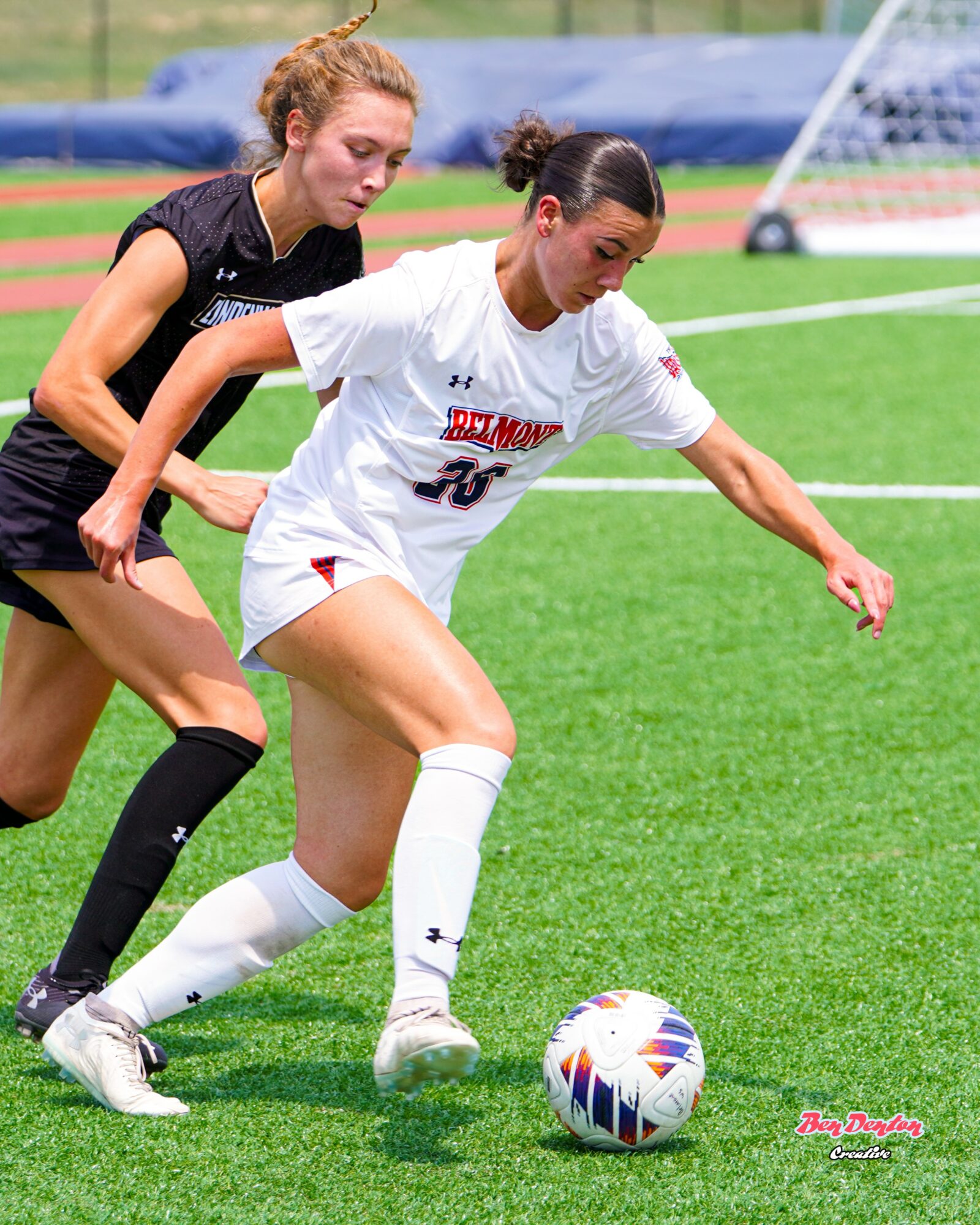 Two female soccer players compete for the ball on a green field during a match.