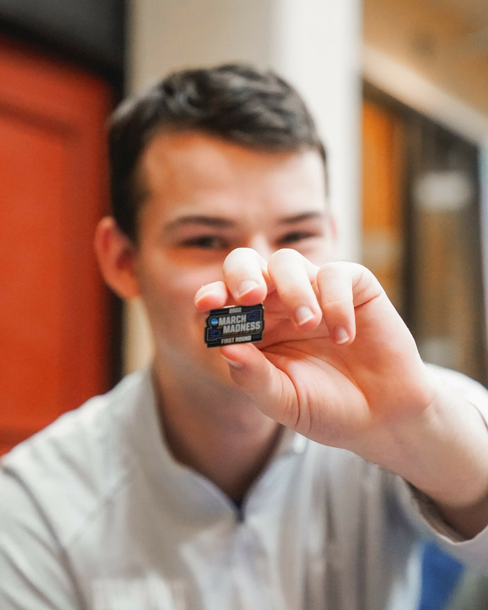 Young person holding a small object close to the camera, with a blurred background, smiling slightly.