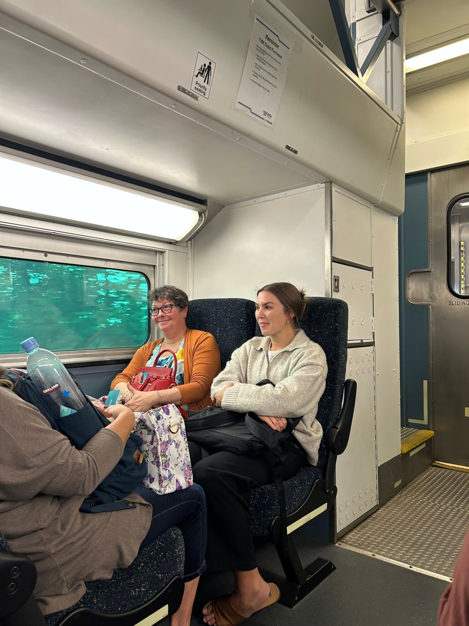 Two women and a child sitting on a train, with the woman in white leaning over the child, who is holding a water bottle.