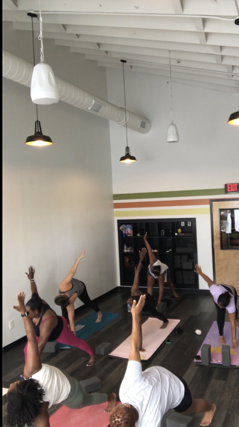 Group of people practicing yoga in a studio with white walls and hanging lights, some in downward dog pose.