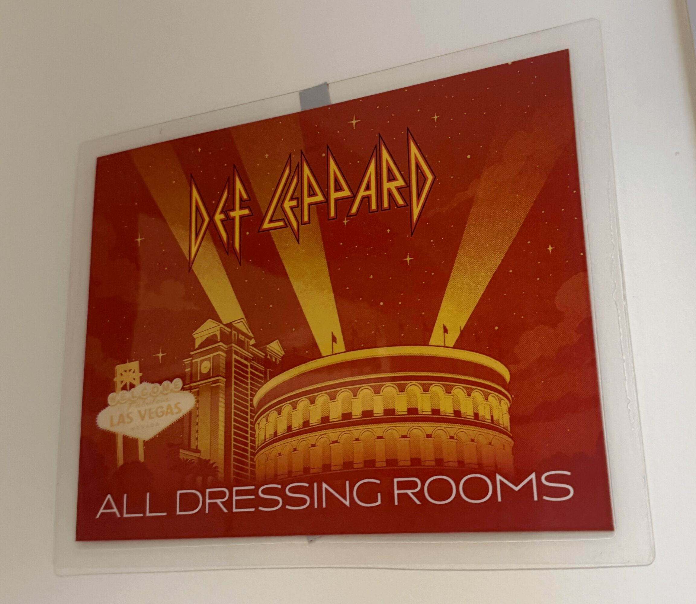 Sign for Def Leppard's all dressing rooms with a red background and yellow beams of light, featuring a circular structure.