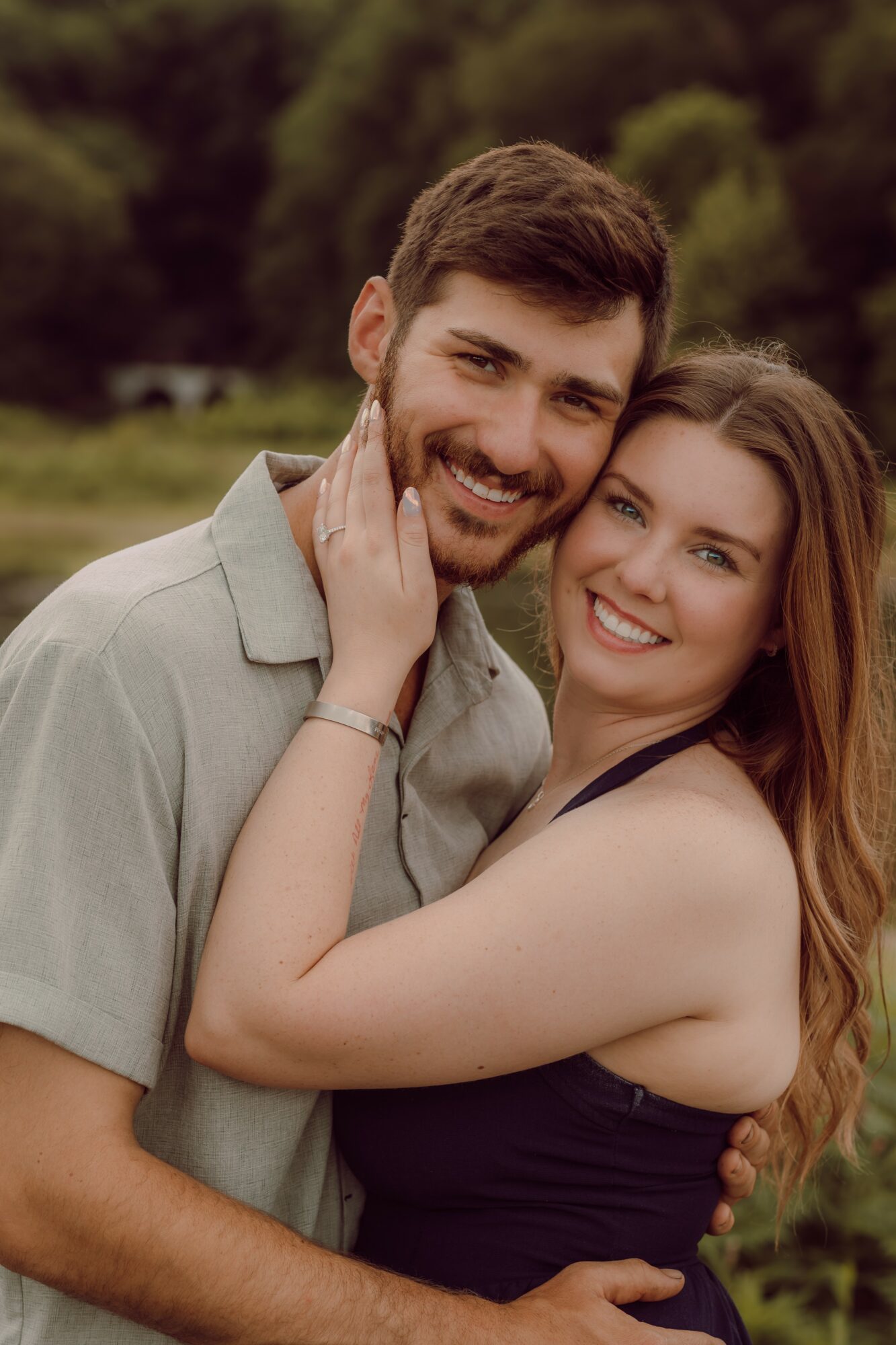 A smiling couple outdoors, the woman touching the man's face, both looking at the camera.