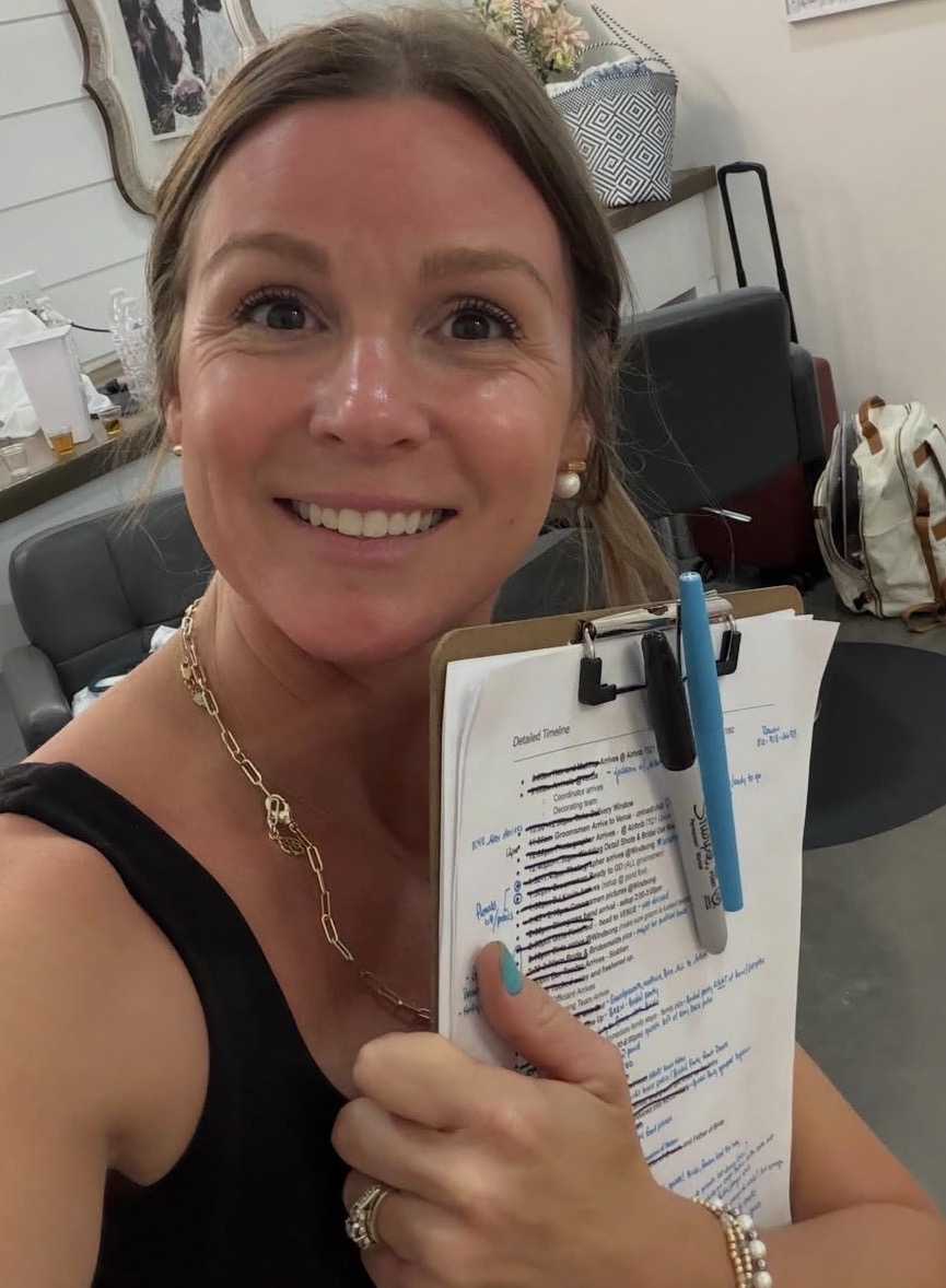Woman smiling, holding a clipboard with papers and a pen, in an office setting.