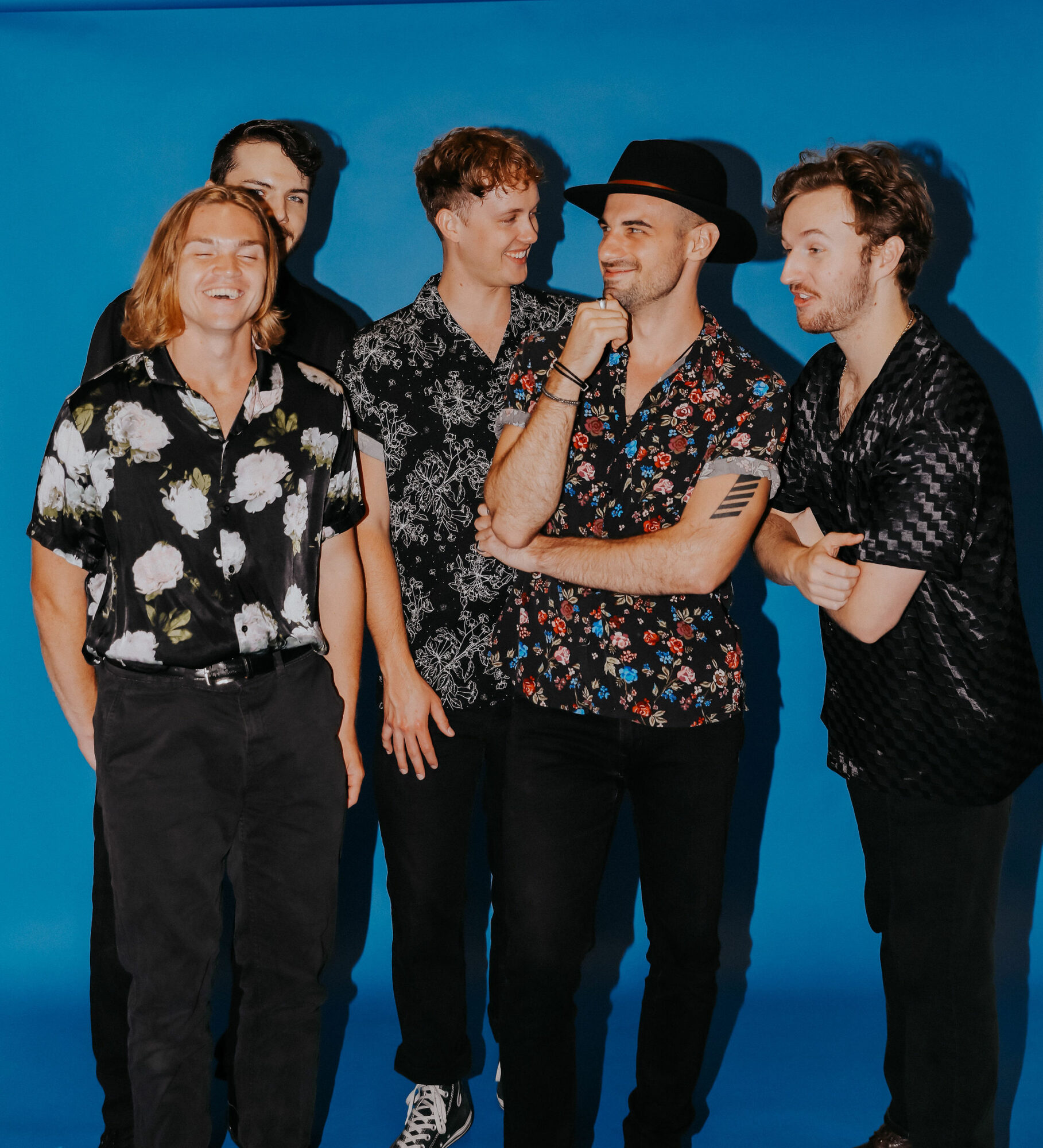 Five people standing together against a blue background, smiling and engaging with each other, dressed in casual clothing.
