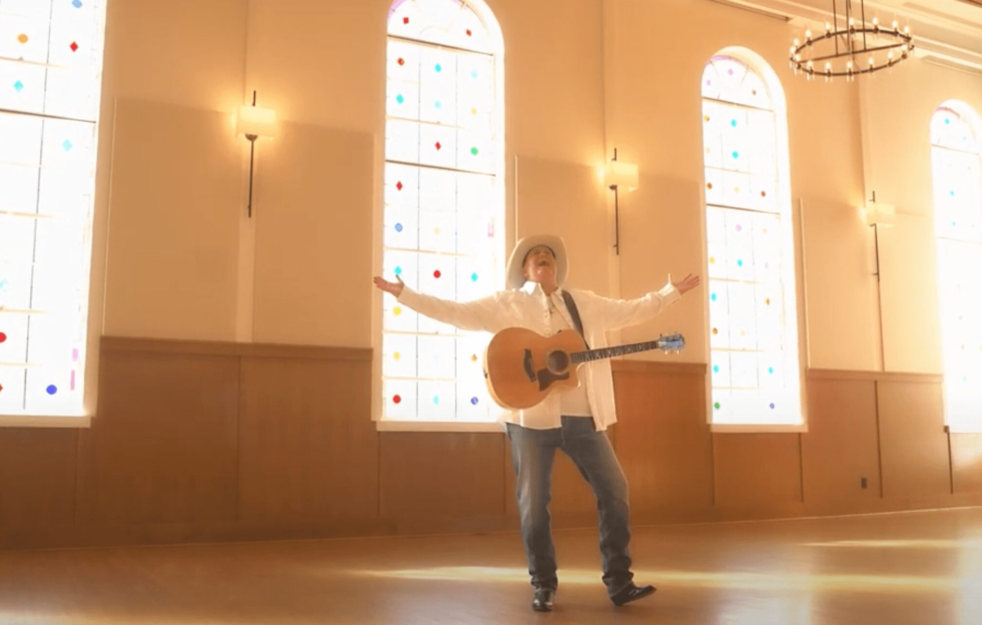 Person playing guitar in a spacious room with tall, arched windows and warm lighting.