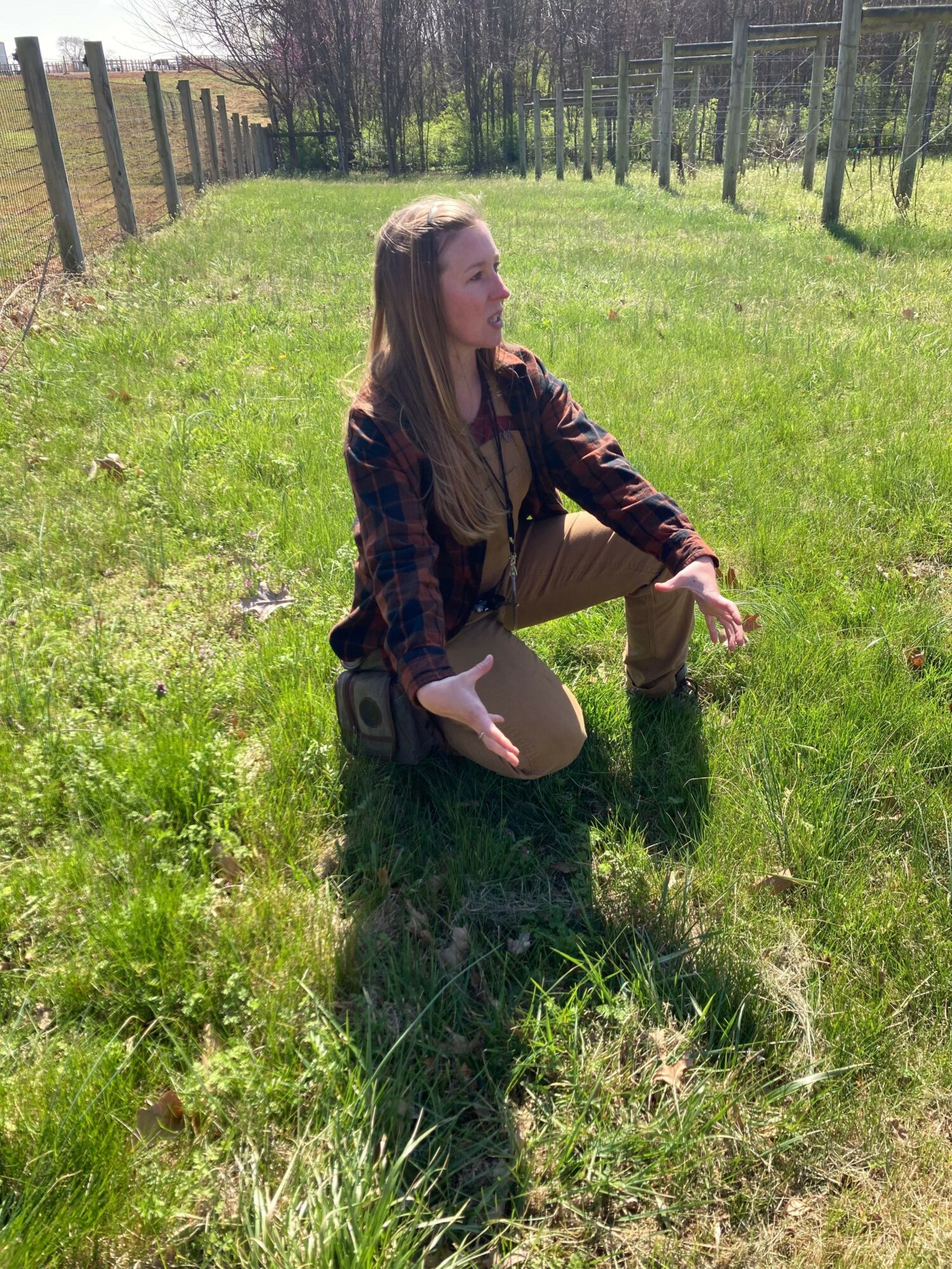 Person sitting on a speaker in a grassy field, surrounded by trees, with one leg crossed and looking to the side.
