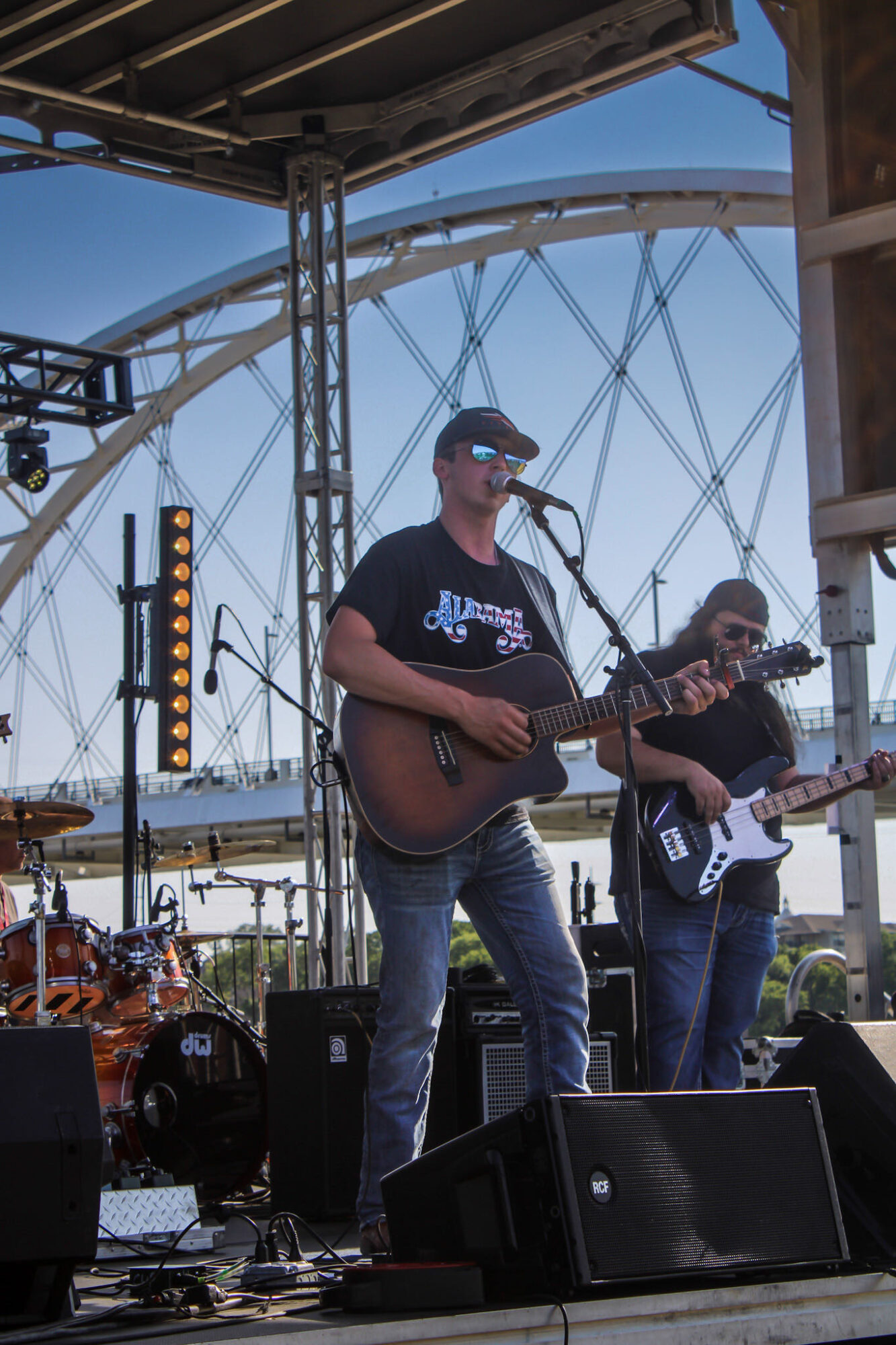 Musicians perform on stage with a large Ferris wheel in the background, playing guitars and singing into microphones.