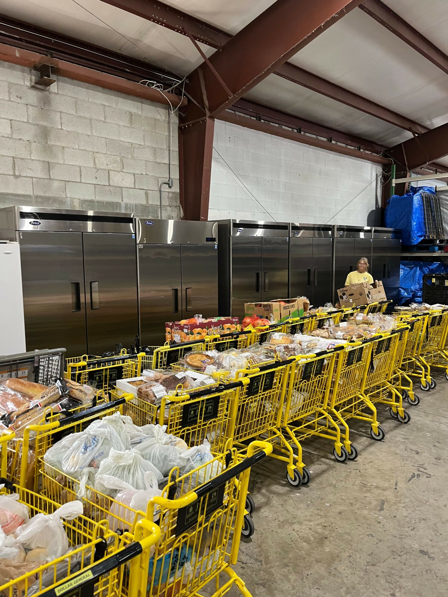 Rows of yellow shopping carts filled with various items, lined up along a concrete floor in a warehouse or store.