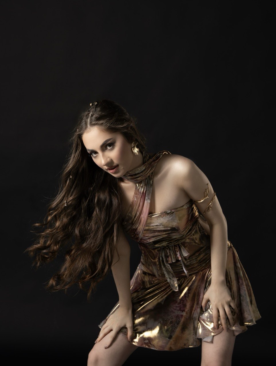 Young woman with long hair in a metallic dress poses against a black background.