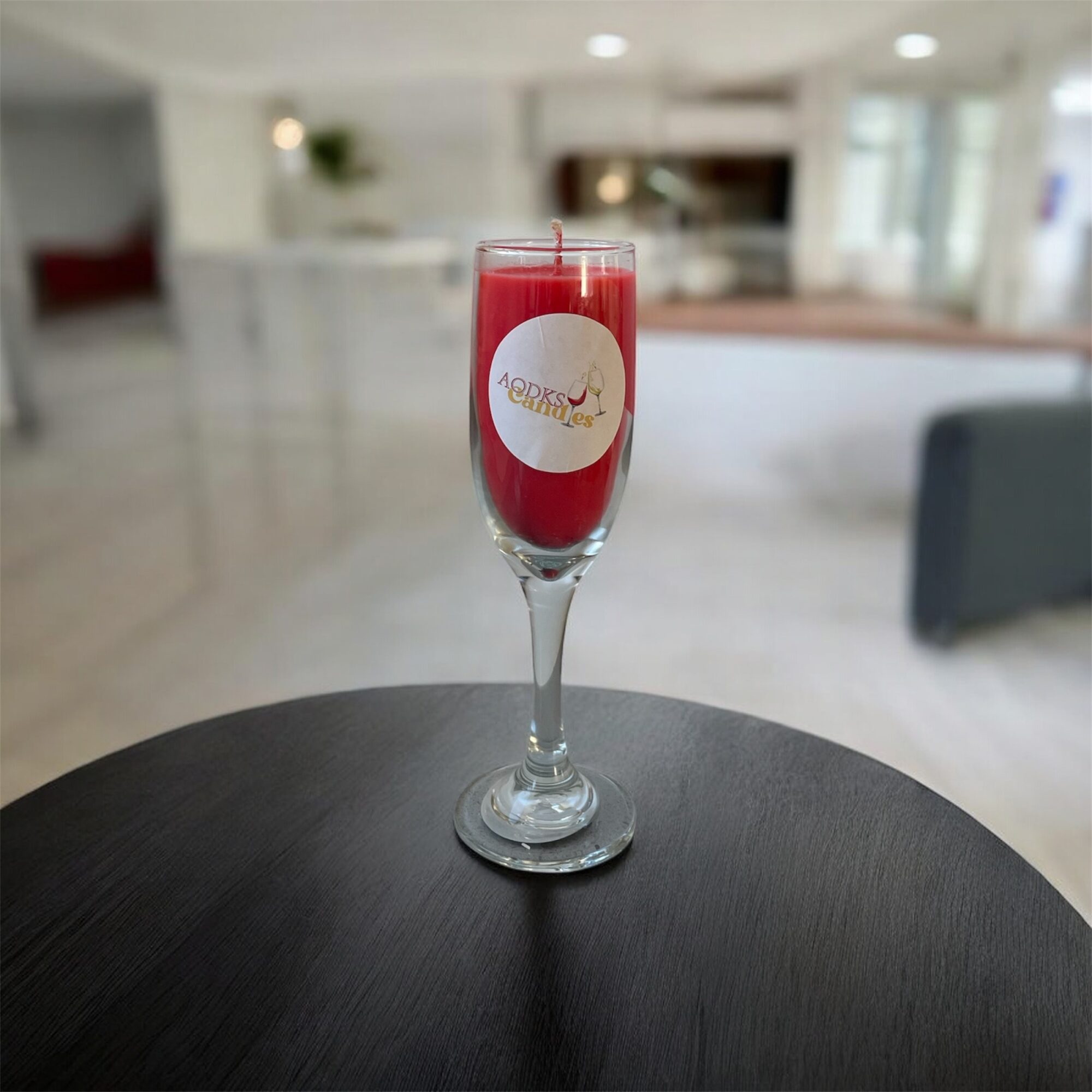 Glass of red beverage with a label, on a dark round table in a bright, modern room.