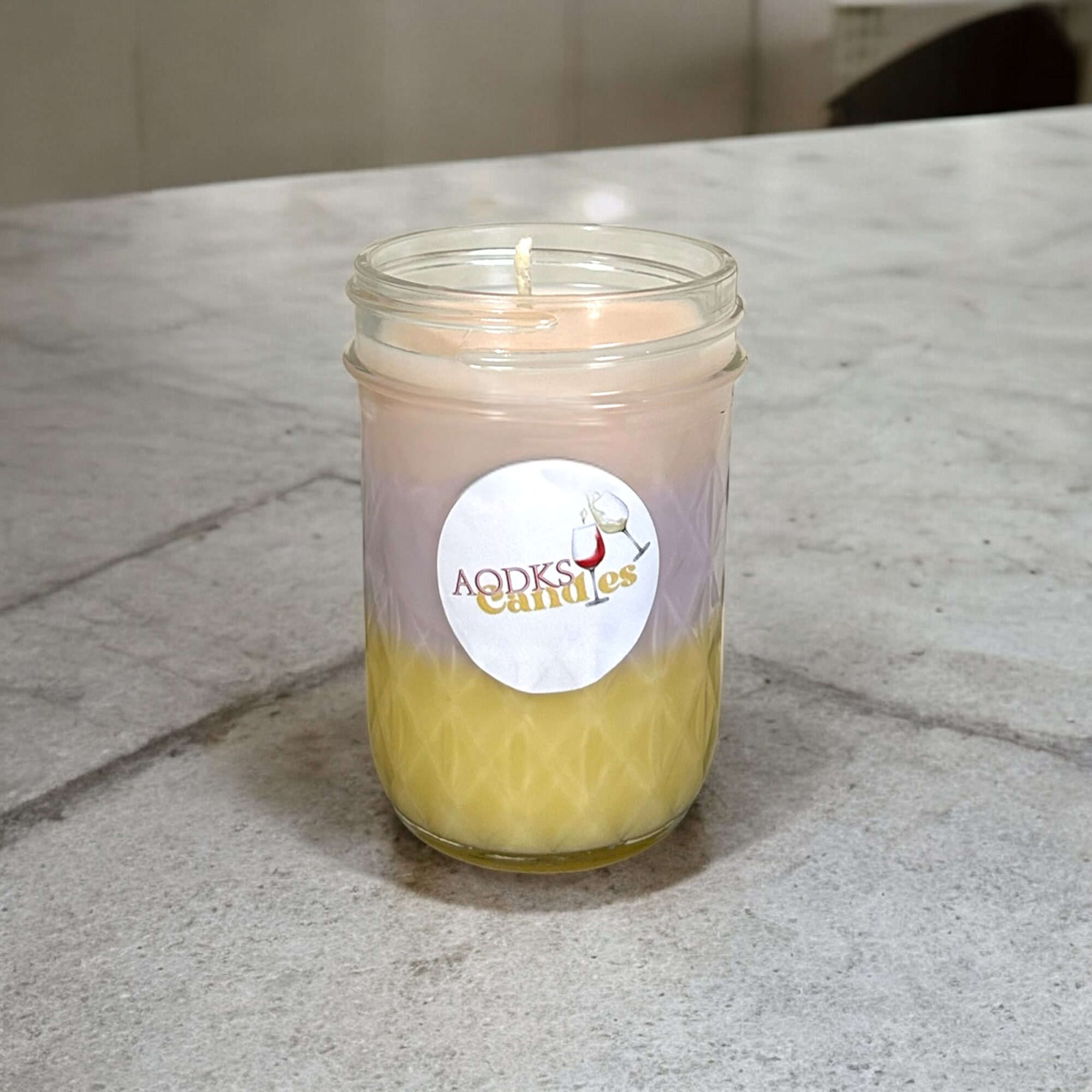 A lit candle in a glass jar with a label, placed on a marble surface.