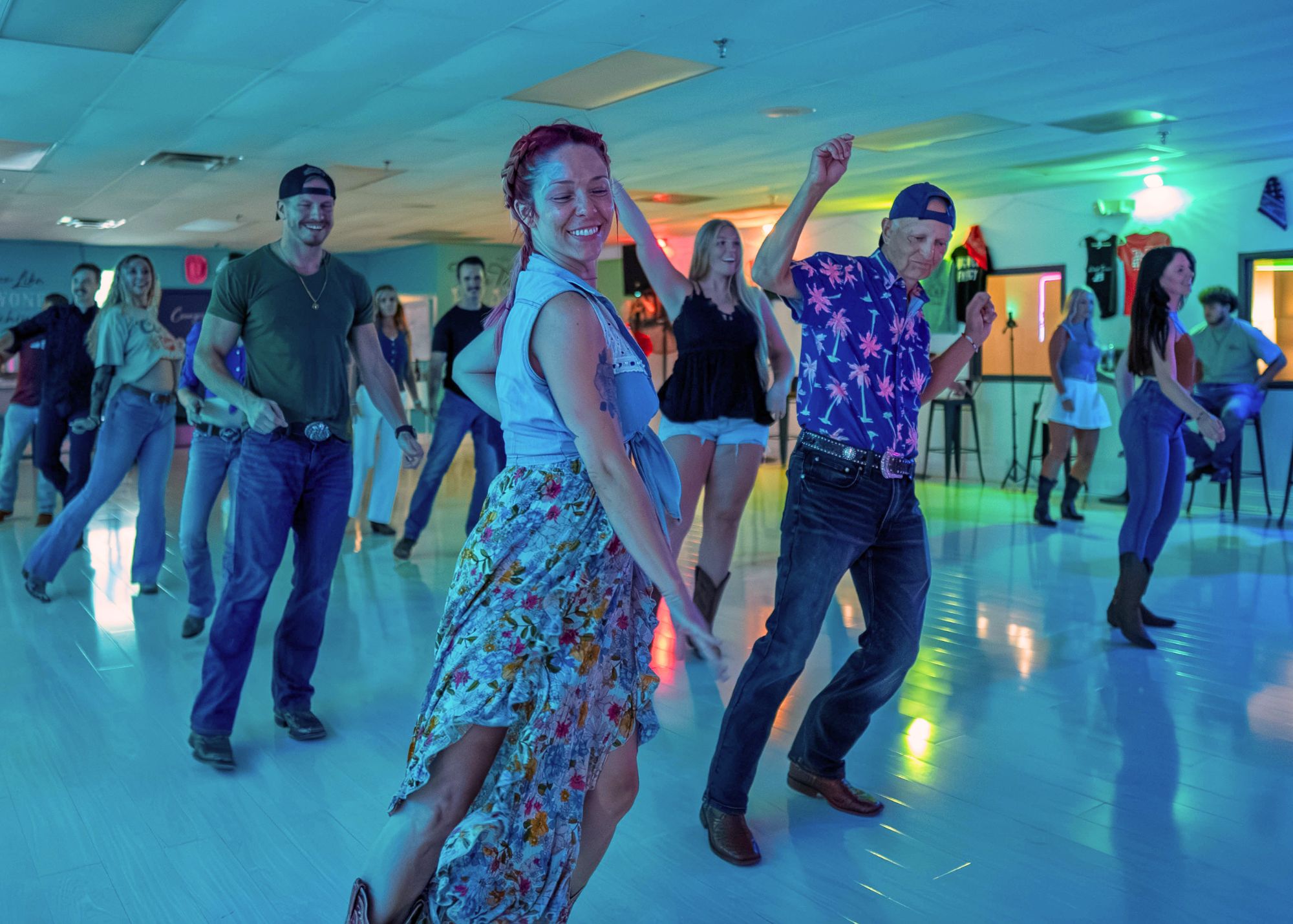 People dancing in a brightly lit indoor space with colorful lights, some smiling and raising their arms.